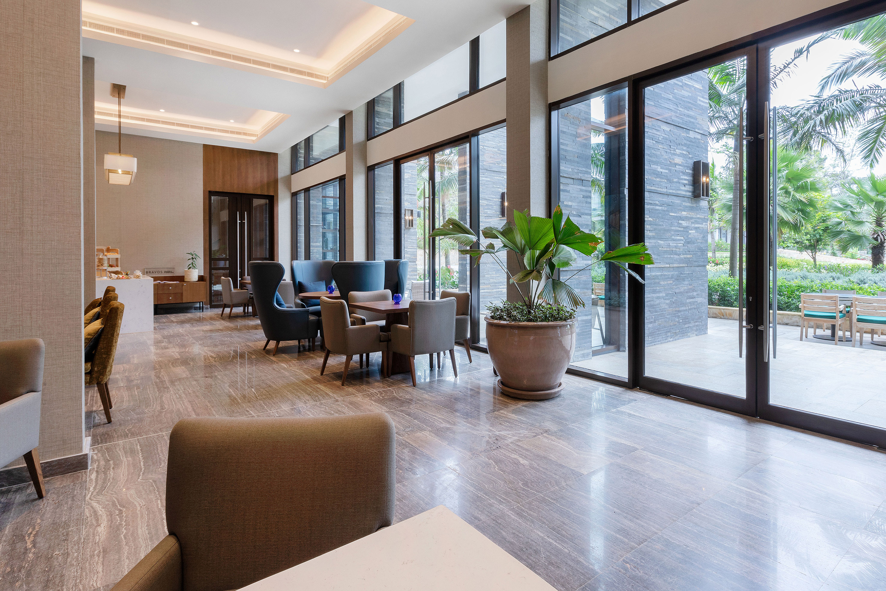 Modern hotel lounge with elegant seating, large windows, and tropical garden view.