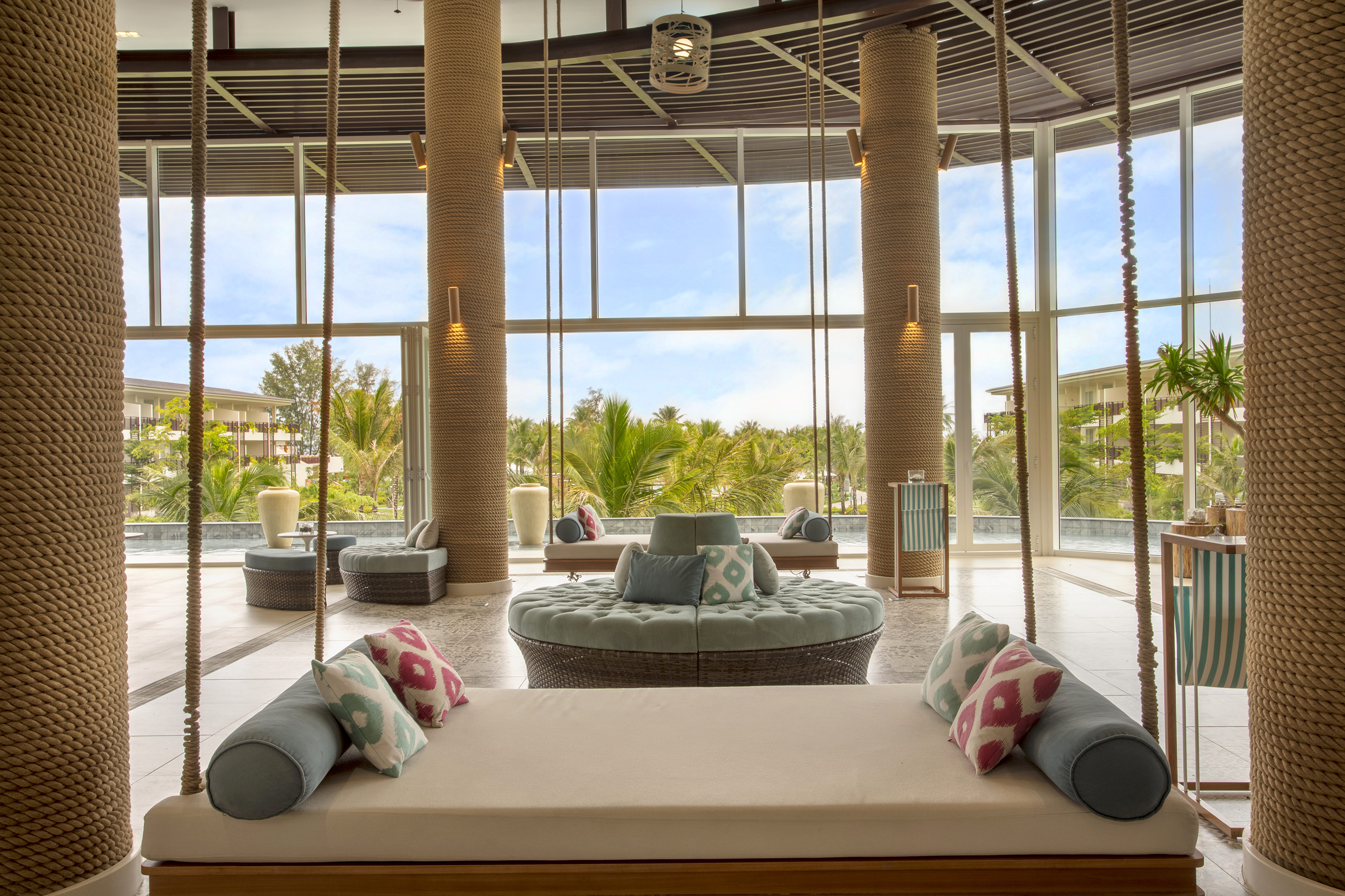 Tropical resort lounge with swing daybeds, rope columns, and garden view.