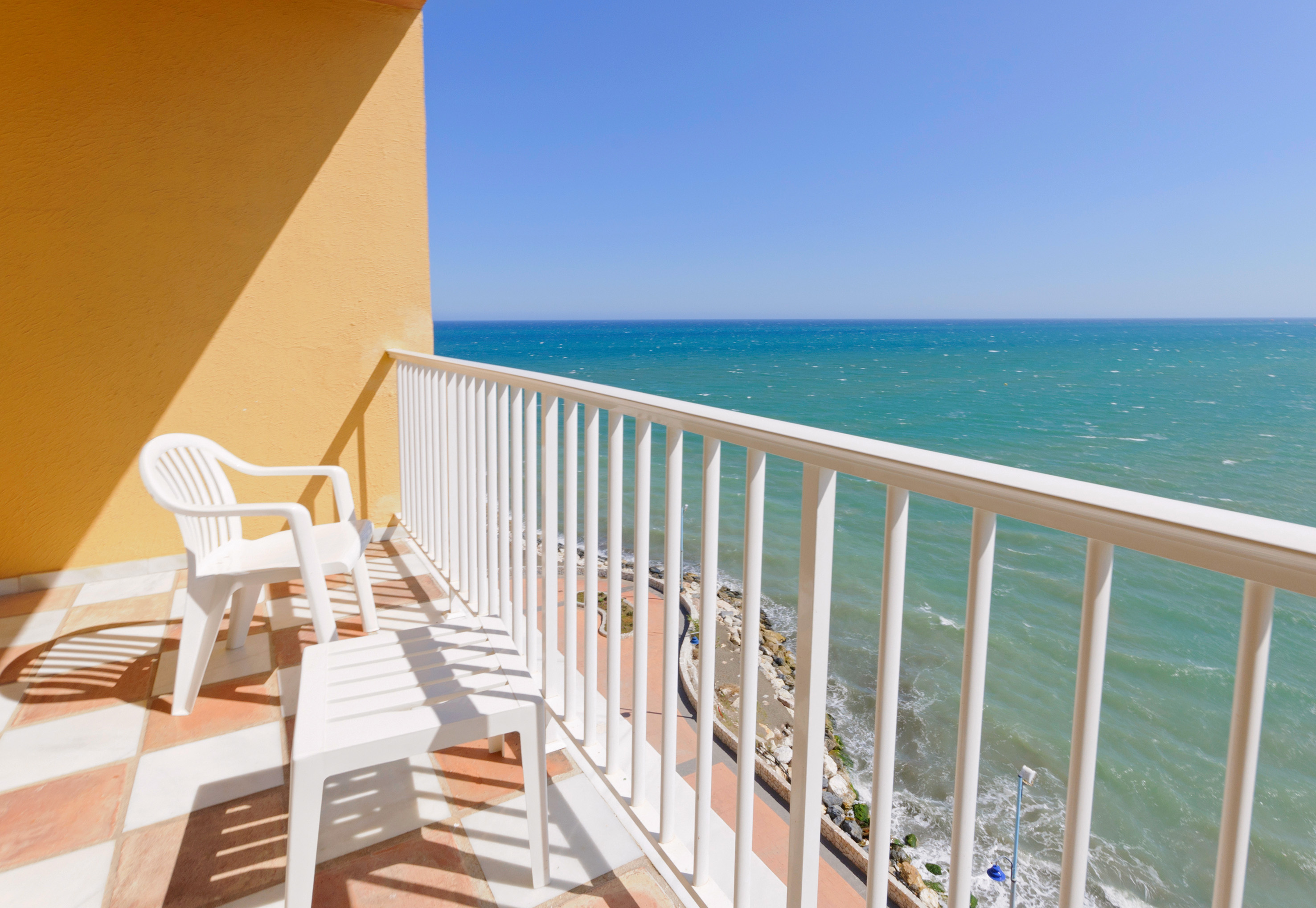 Sunny balcony with white chairs, table, and turquoise ocean view.