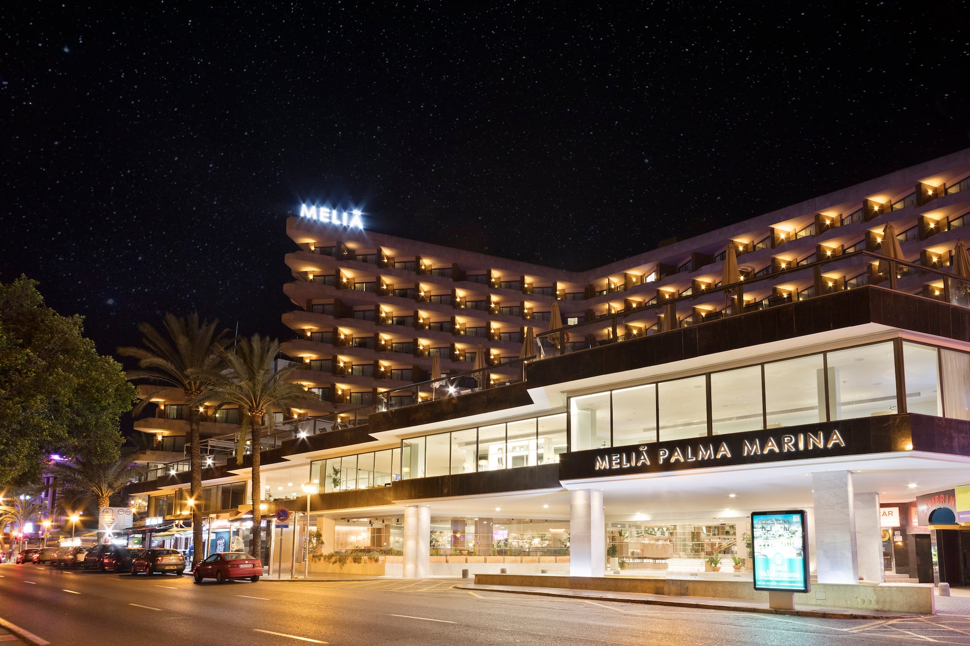 Melia Palma Marina hotel at night, illuminated under a starry sky, with palm trees.
