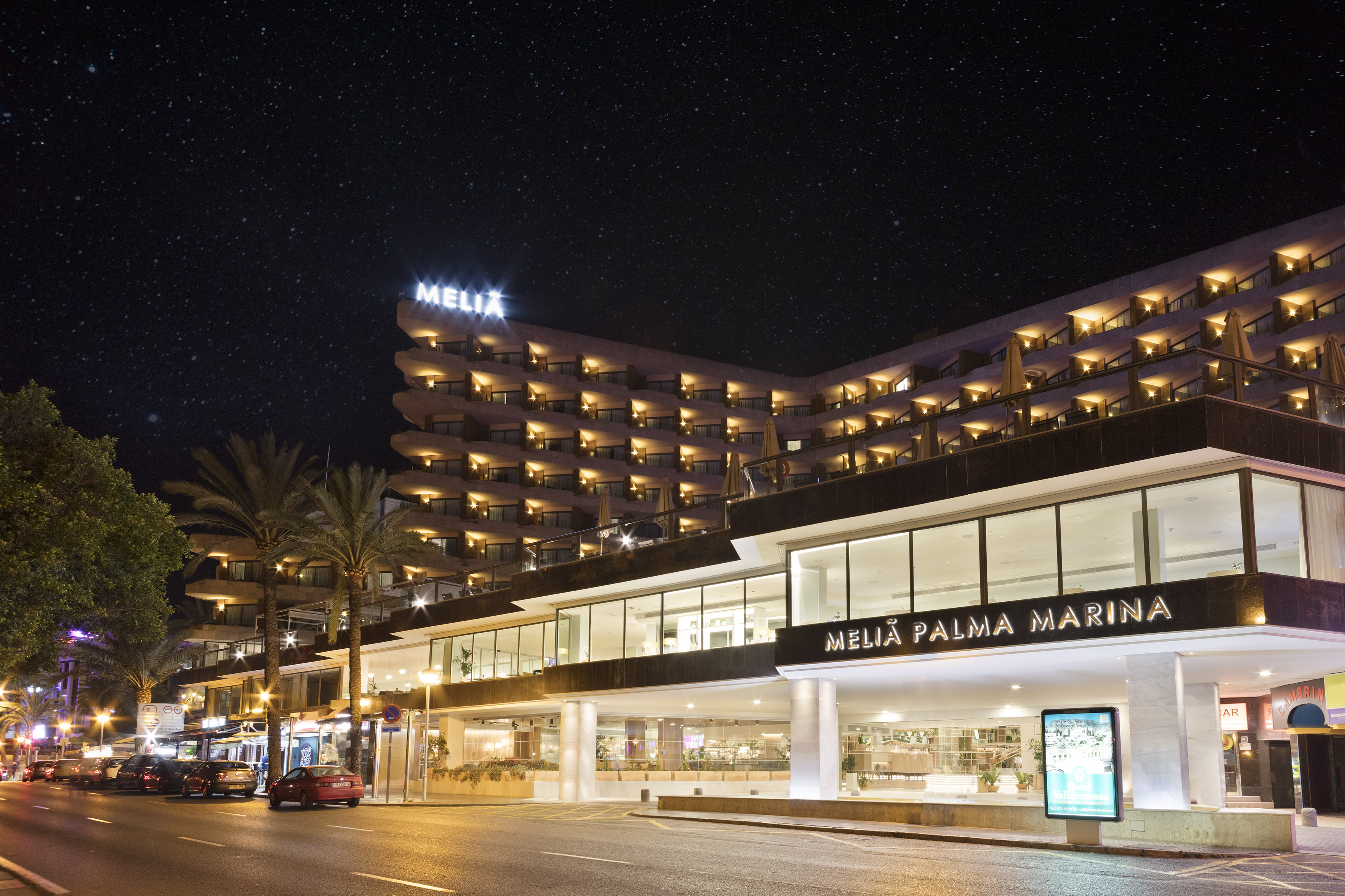 Melia Palma Marina hotel at night, illuminated under a starry sky, with palm trees.