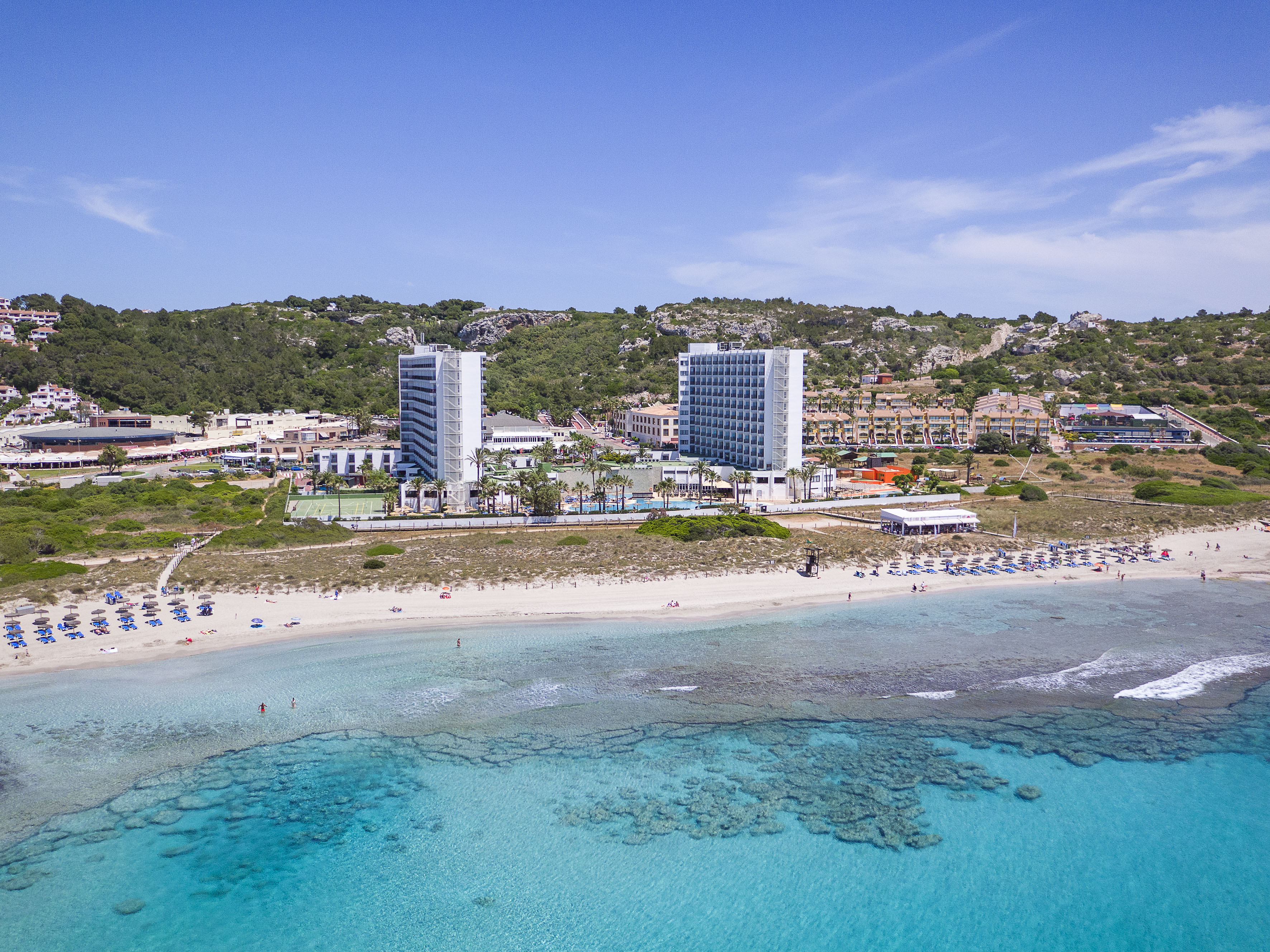 Aerial view of beachfront hotels, sandy beach, and clear turquoise water.