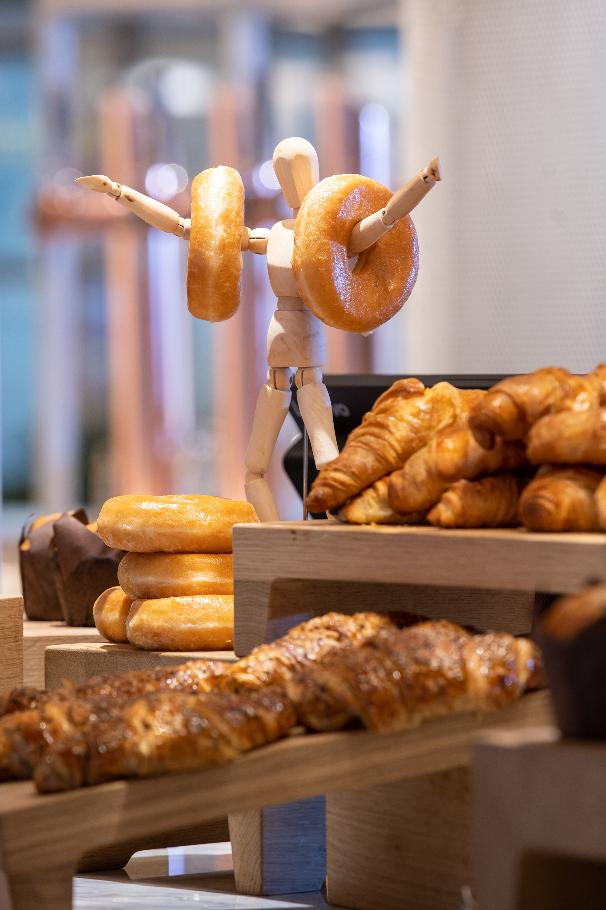 Wooden mannequin lifting glazed donuts, fresh pastries, and croissants on display.