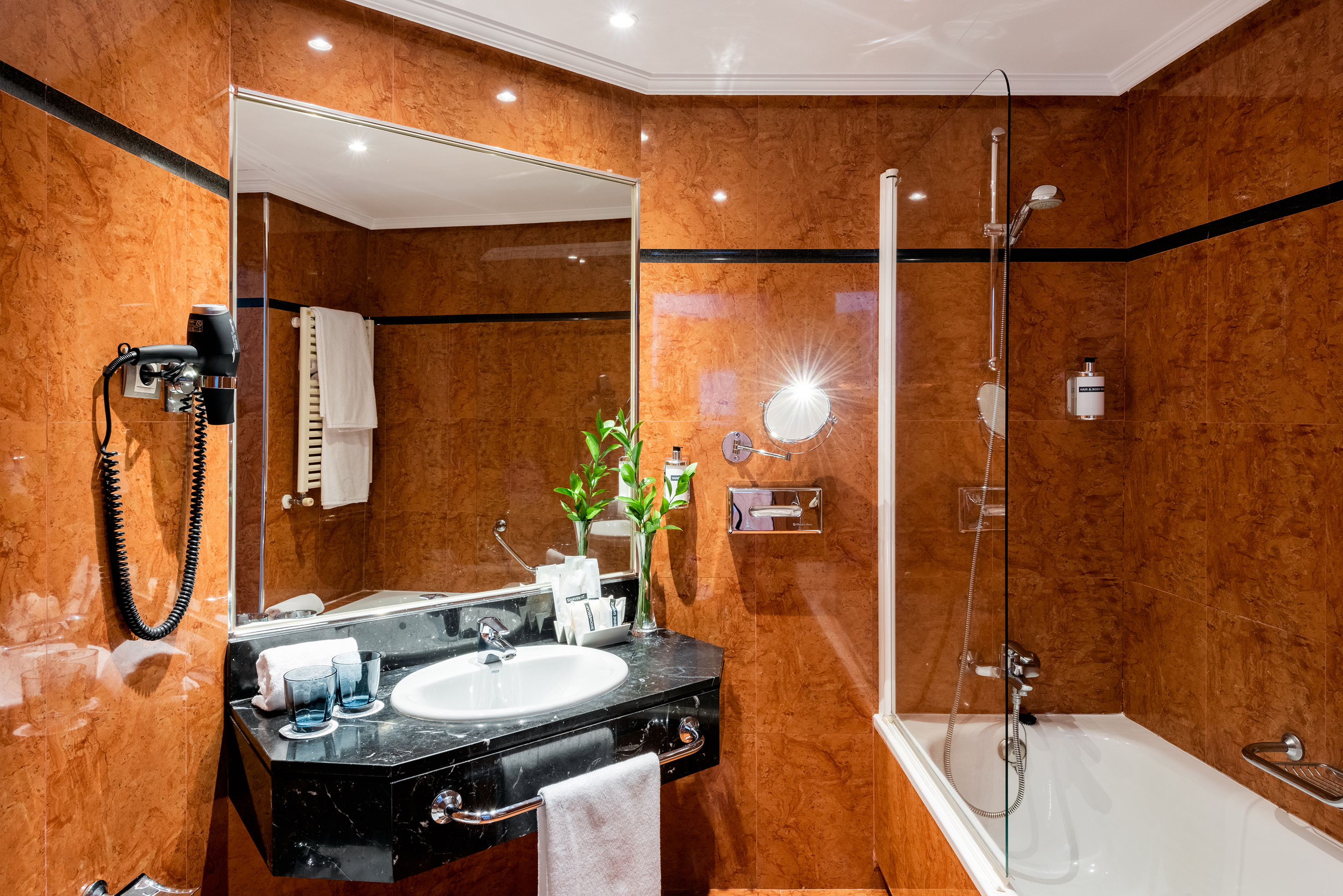 Modern hotel bathroom with brown marble, vanity, shower, and bathtub.