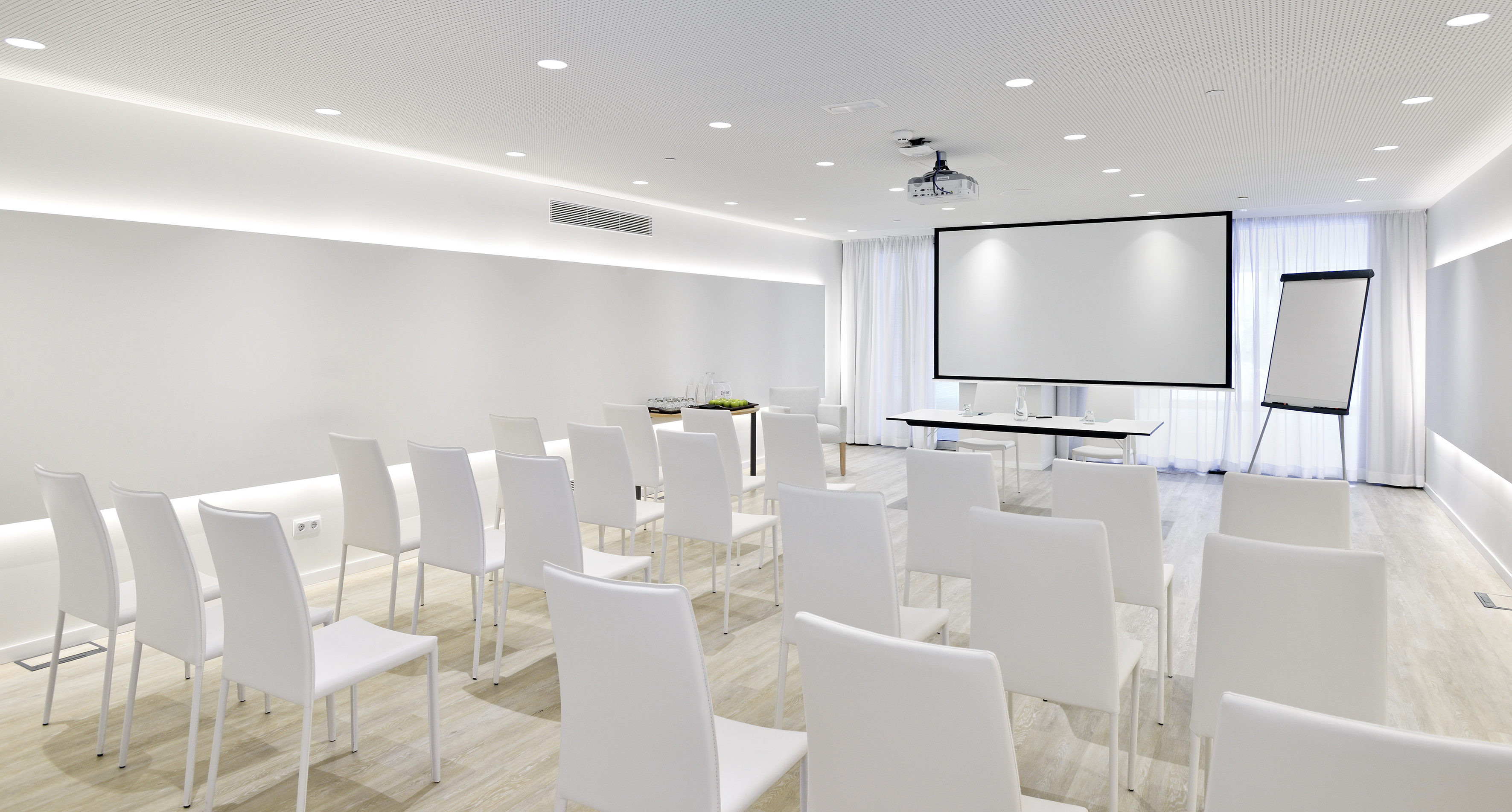 Modern meeting room with projector screen, white chairs, and flipchart.