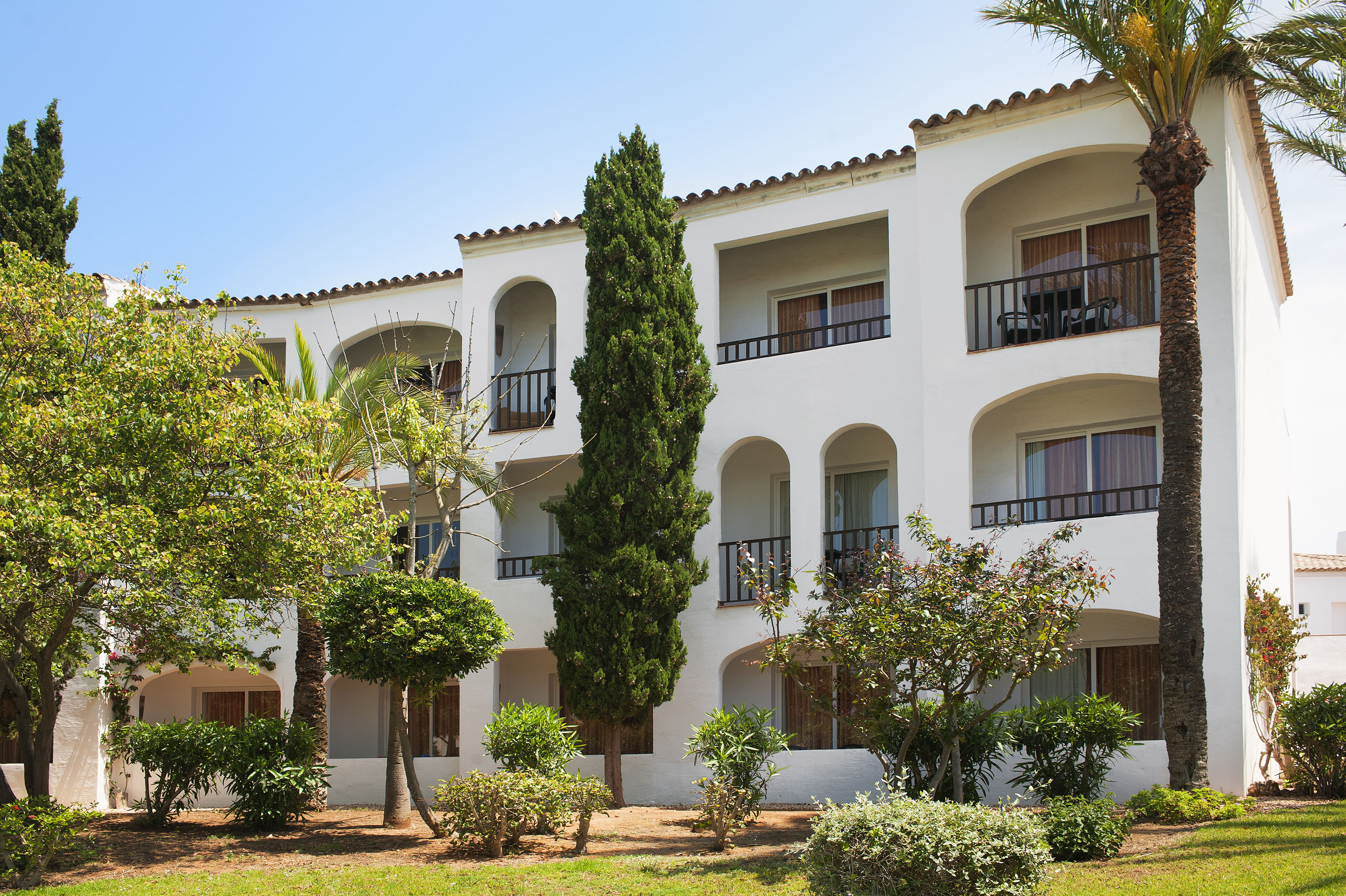White Mediterranean hotel, arched balconies, palm trees, sunny garden.