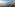 Blue fishing boats on a sandy beach fronting a colorful cliffside town and ocean.