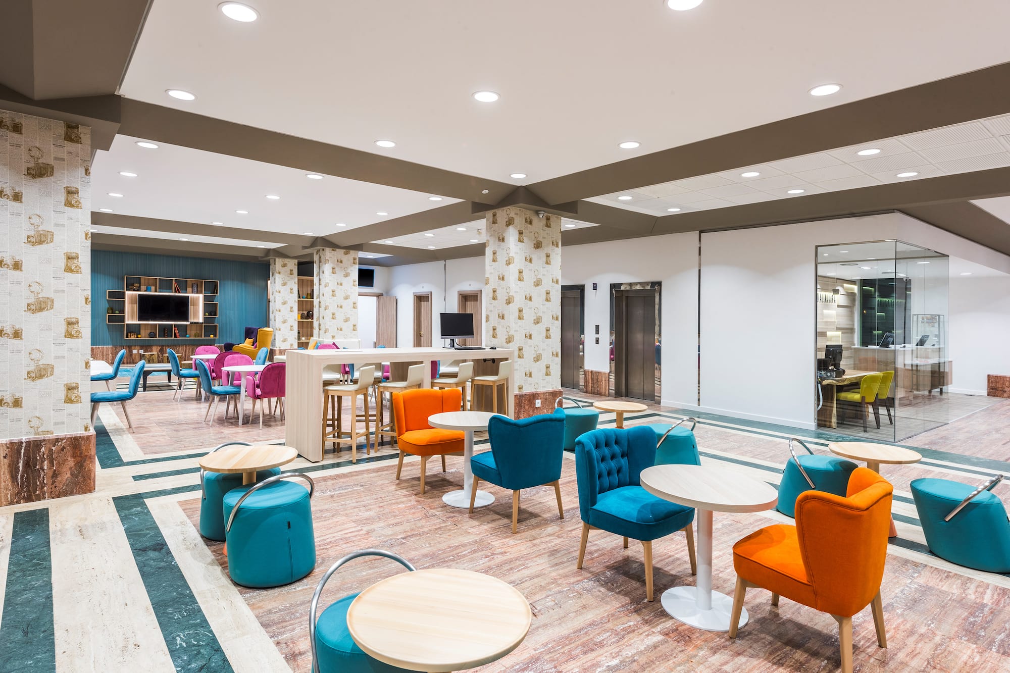 Modern hotel lounge with colorful seating, small tables, and striped flooring.