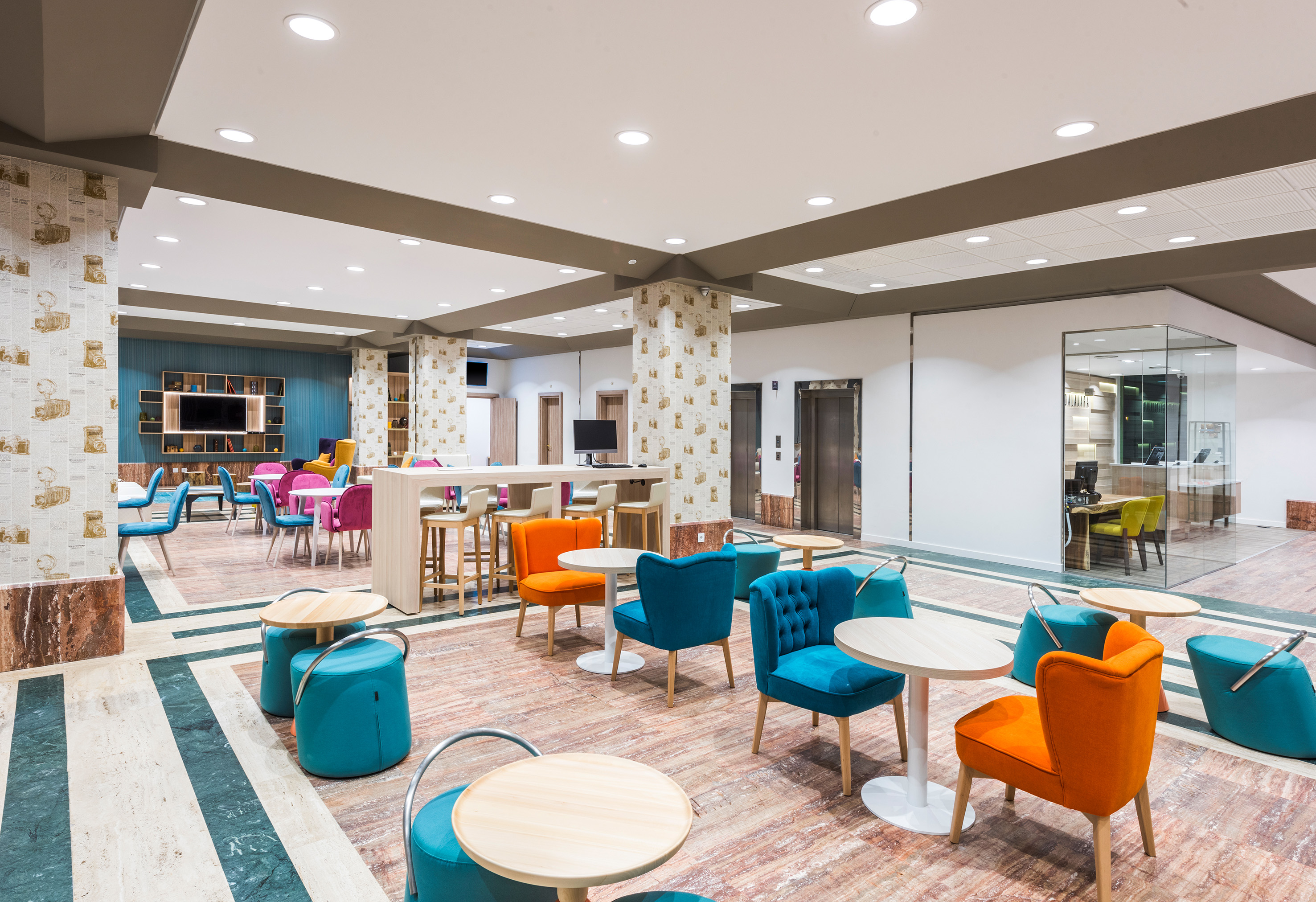 Modern hotel lounge with colorful seating, small tables, and striped flooring.