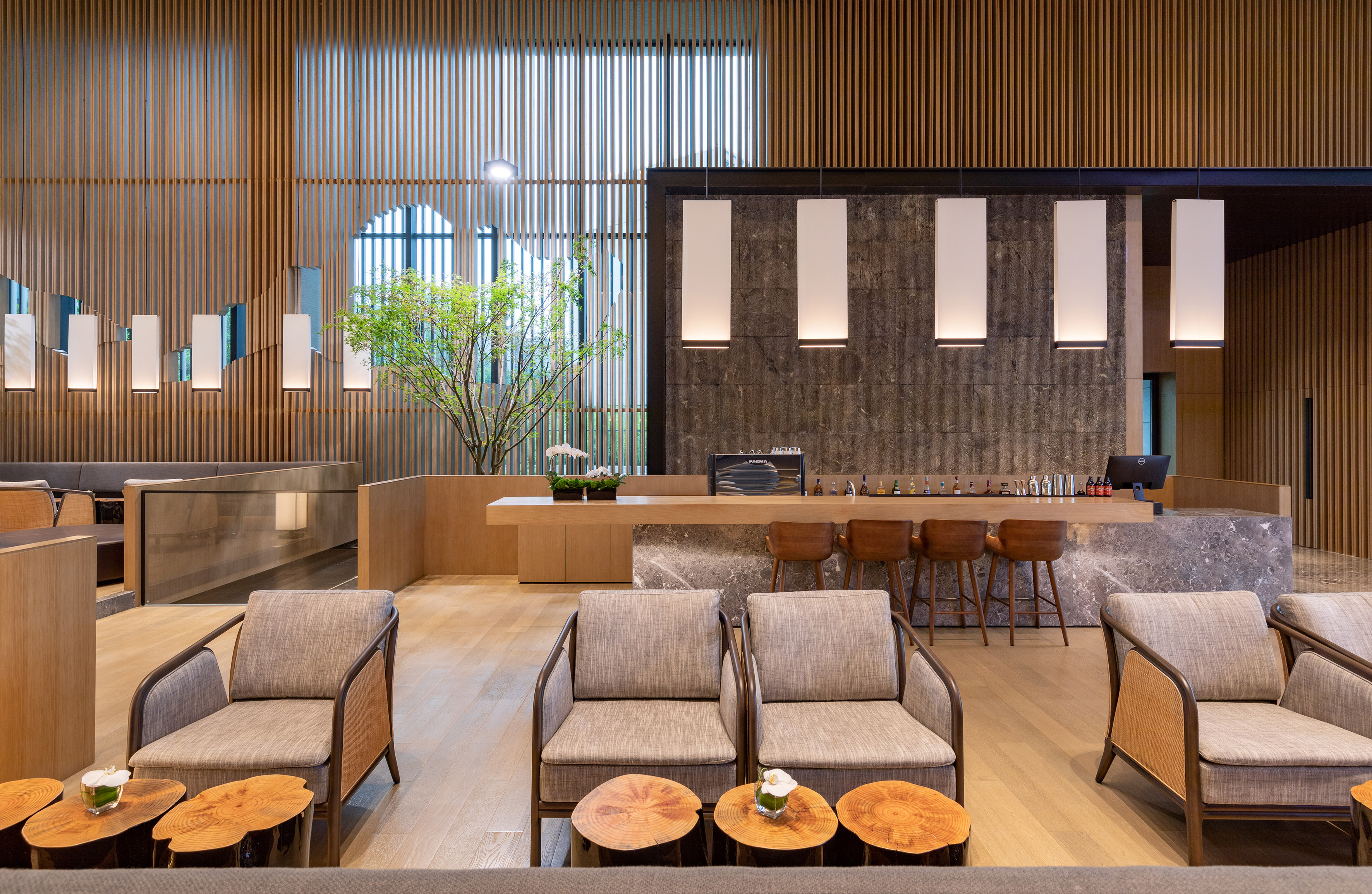 Modern lounge bar. Wood screens, marble counter, fabric chairs, and green plant.