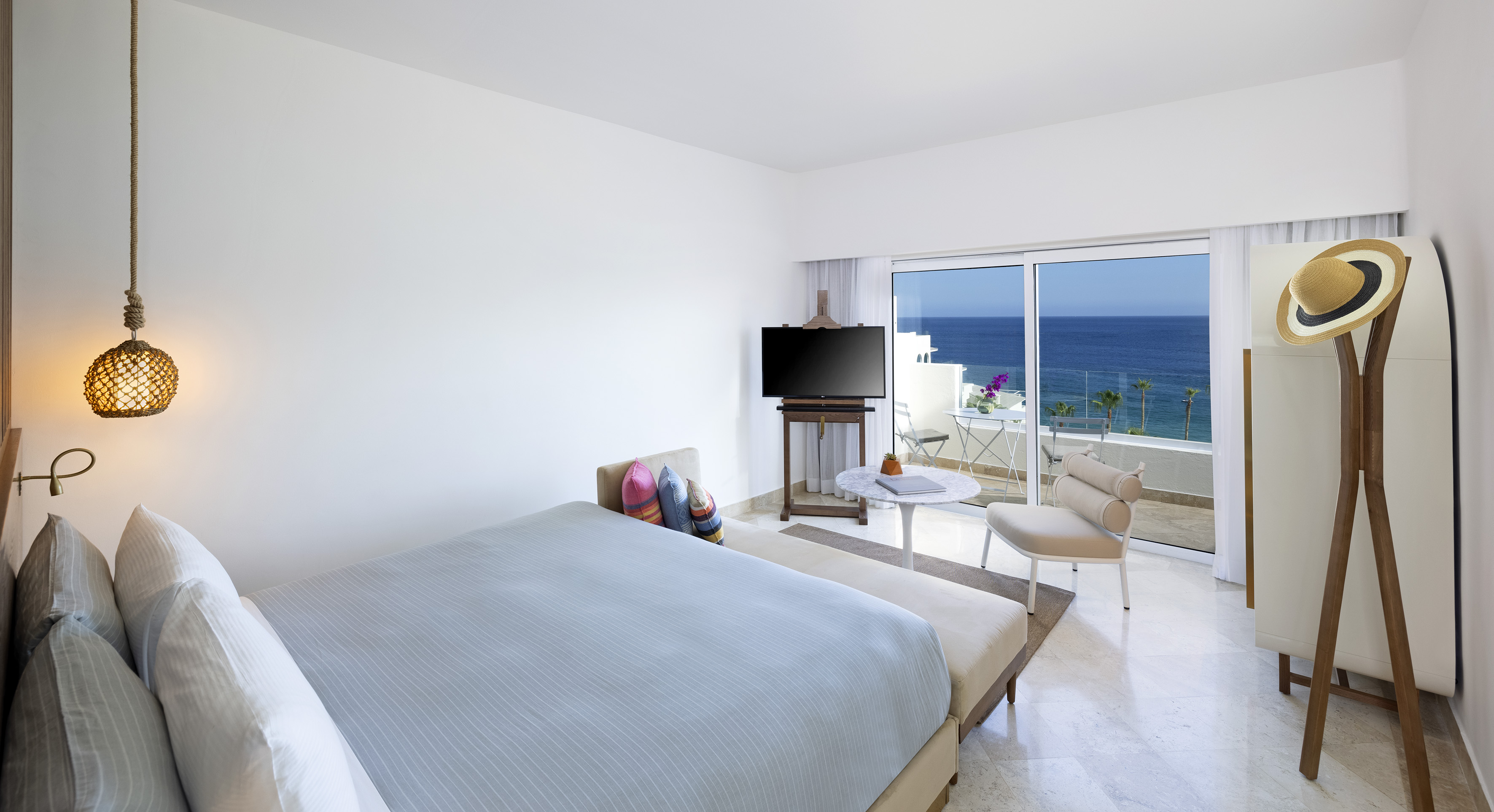 Modern resort room with ocean view balcony, large bed, and white decor.