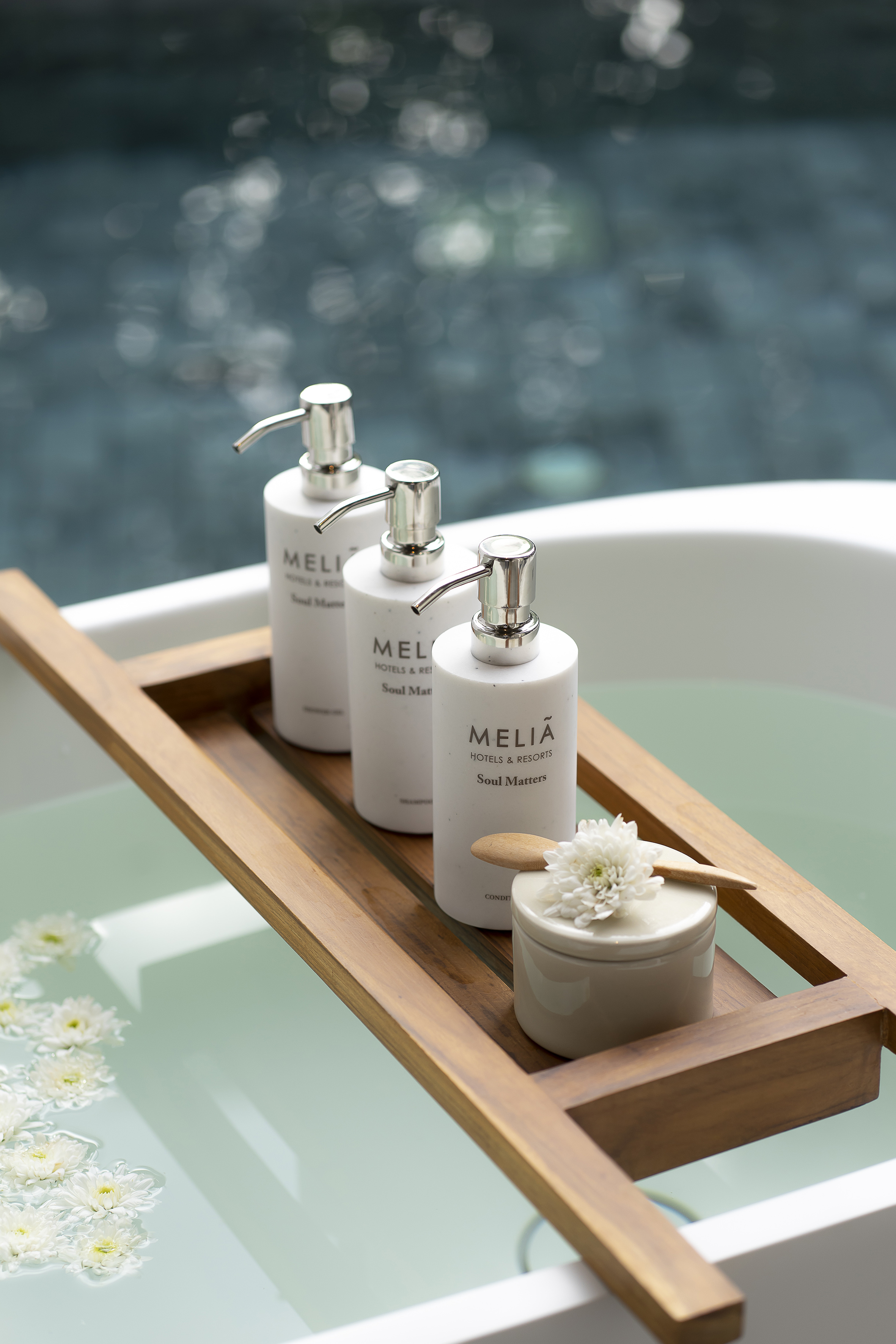 Meliá Hotels Soul Matters bath products on wooden caddy in luxury tub with flowers.