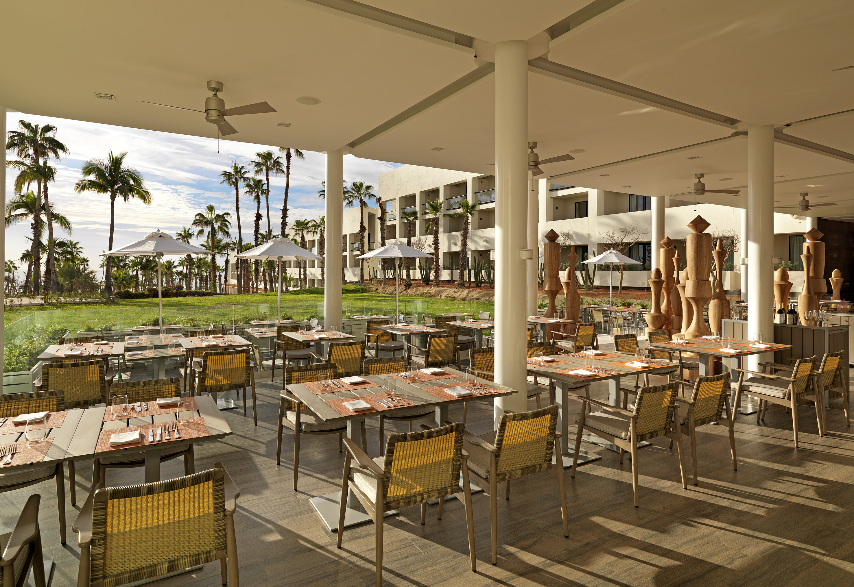 Resort open-air dining terrace overlooking palm trees and green lawn.