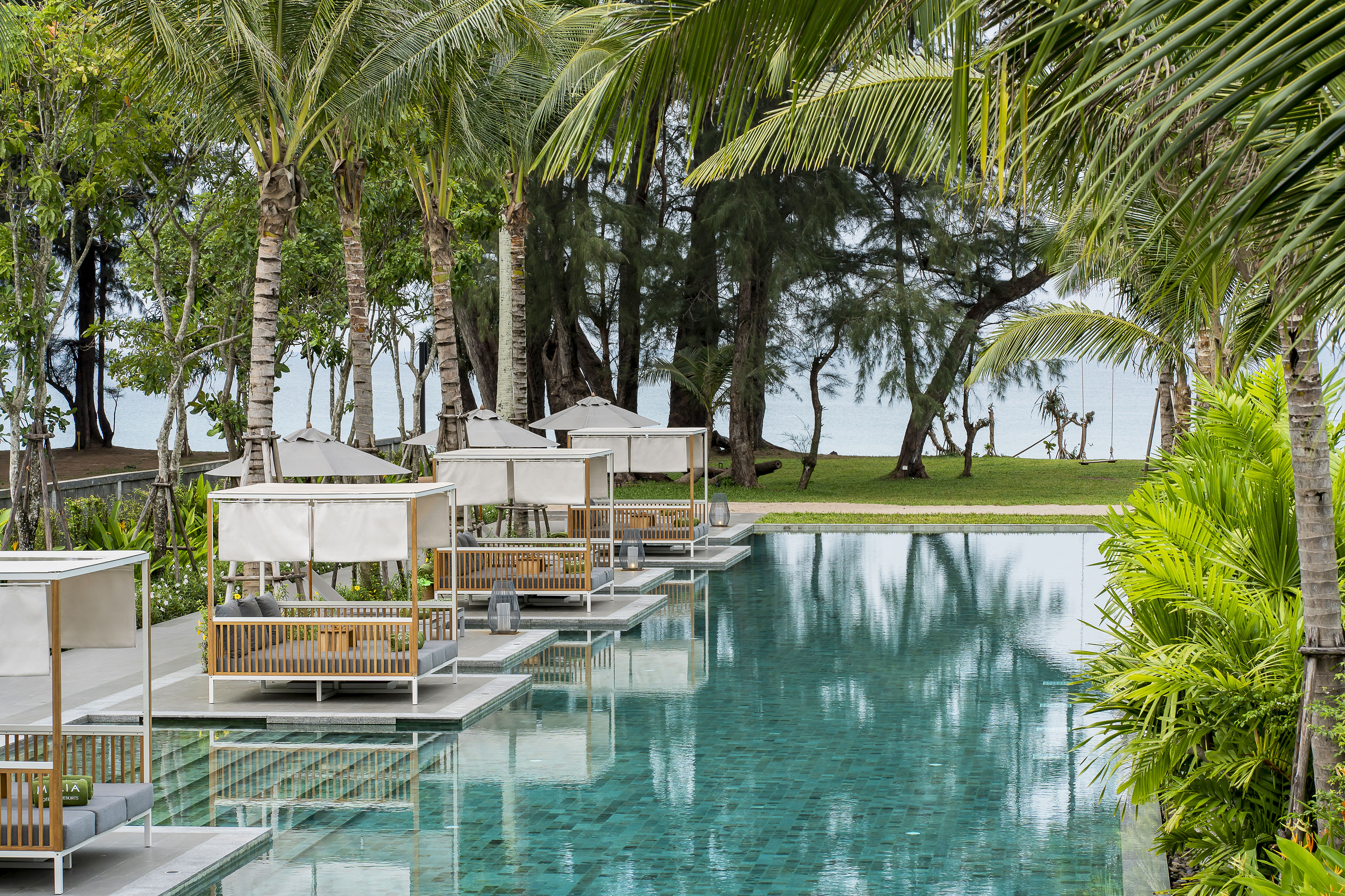 Beachfront resort pool with elegant cabanas, palm trees, and turquoise water.