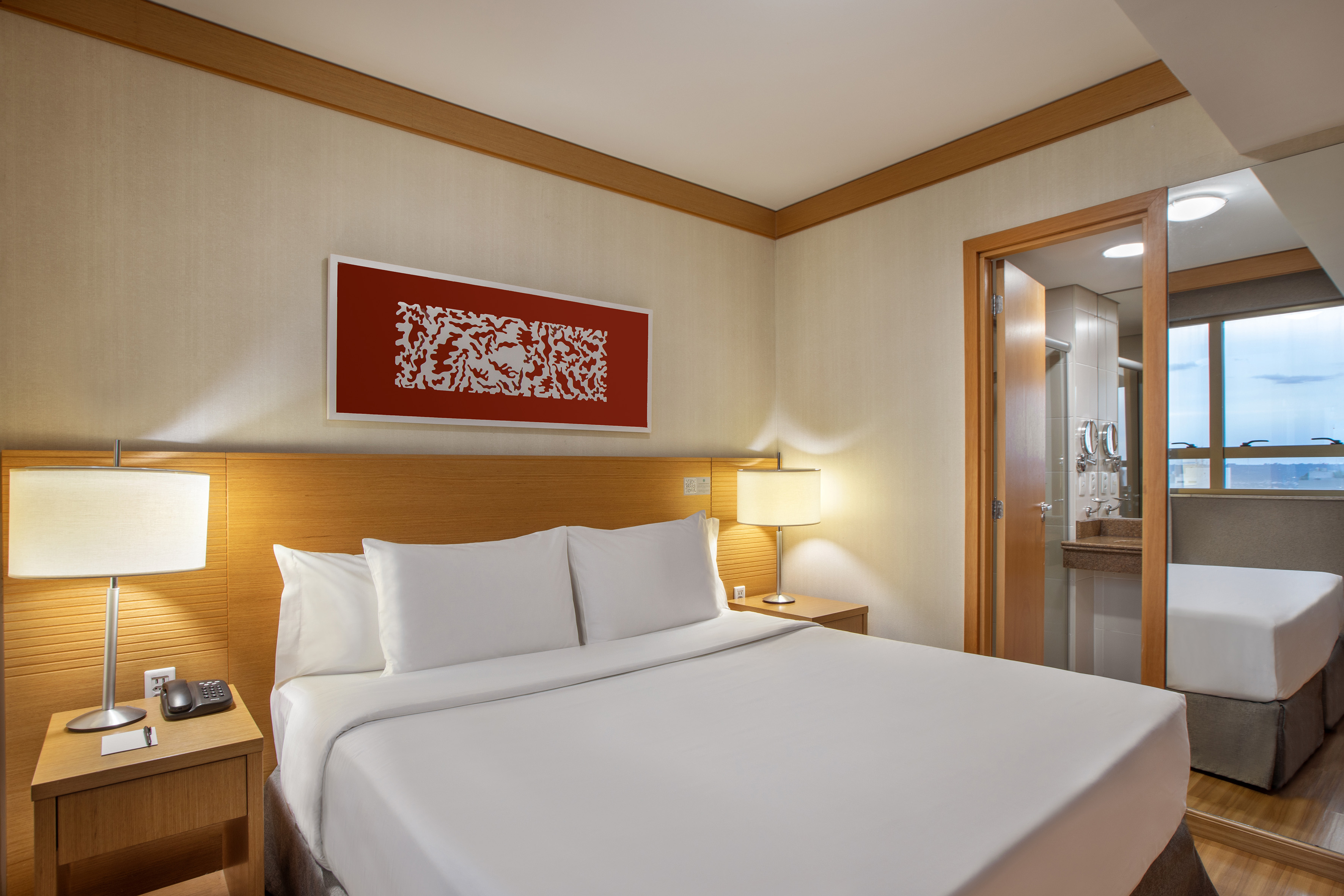 Hotel bedroom with large bed, white linens, wooden nightstands, red artwork.