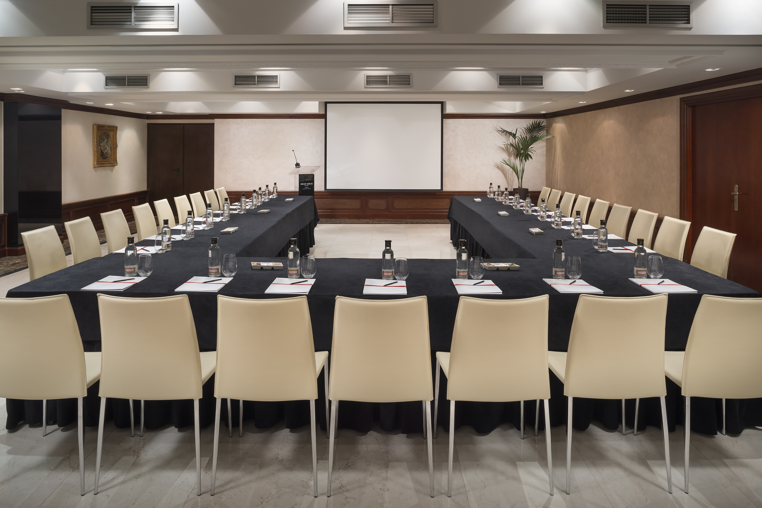 U-shaped conference room with screen, lectern, tables, and cream chairs.