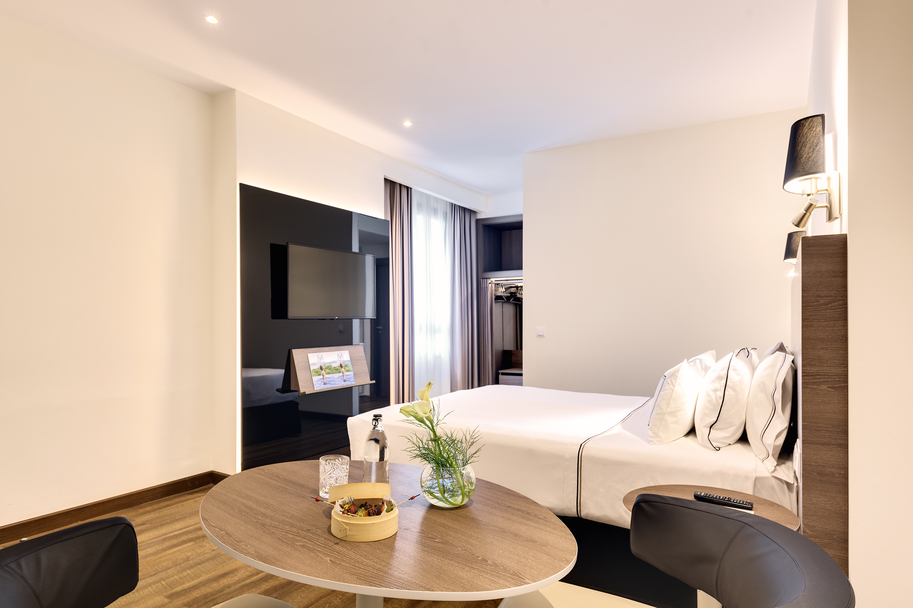 Contemporary hotel suite with white bed, TV, and lounge area.