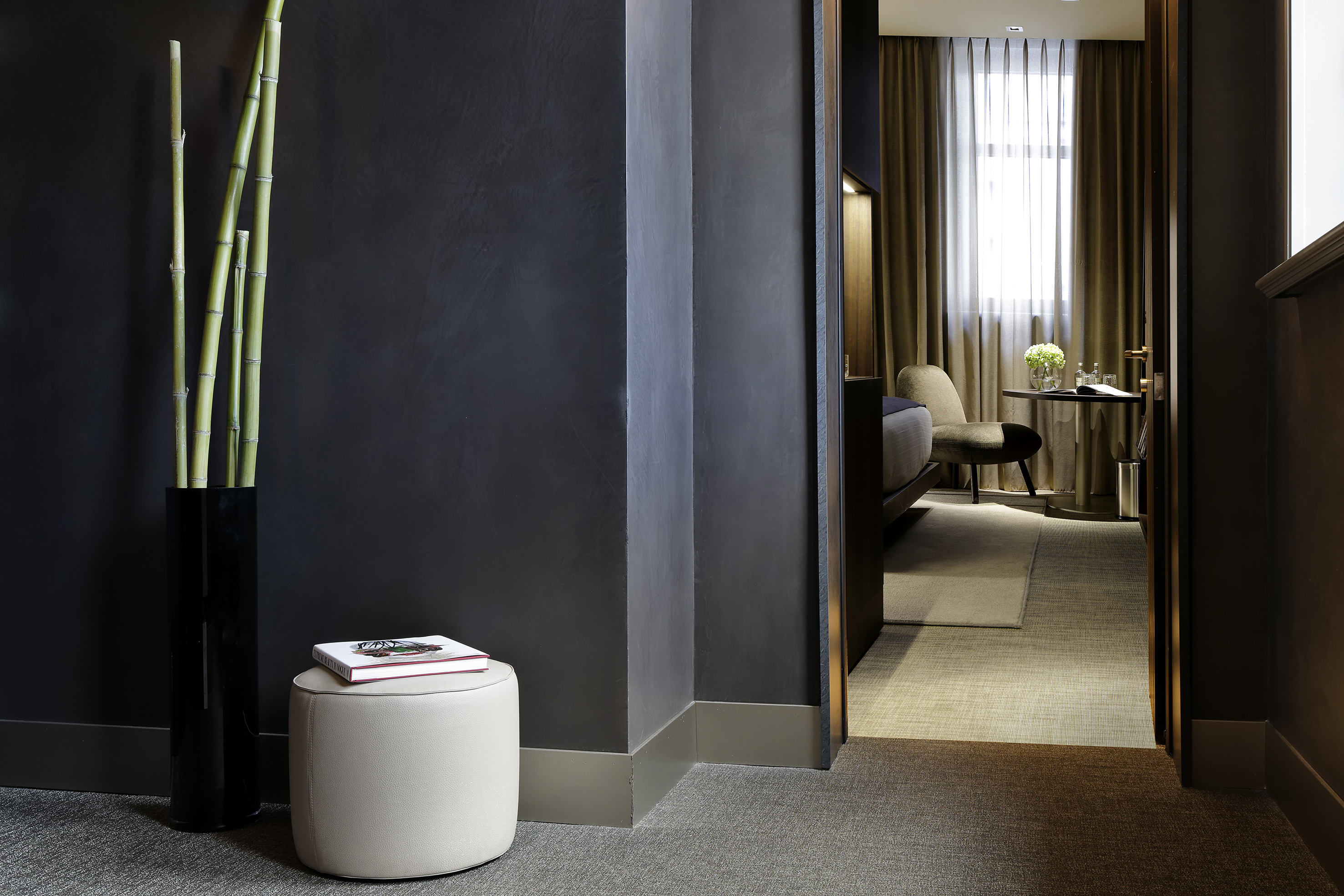 Modern hotel room entry with bamboo, ottoman, and elegant bedroom view.