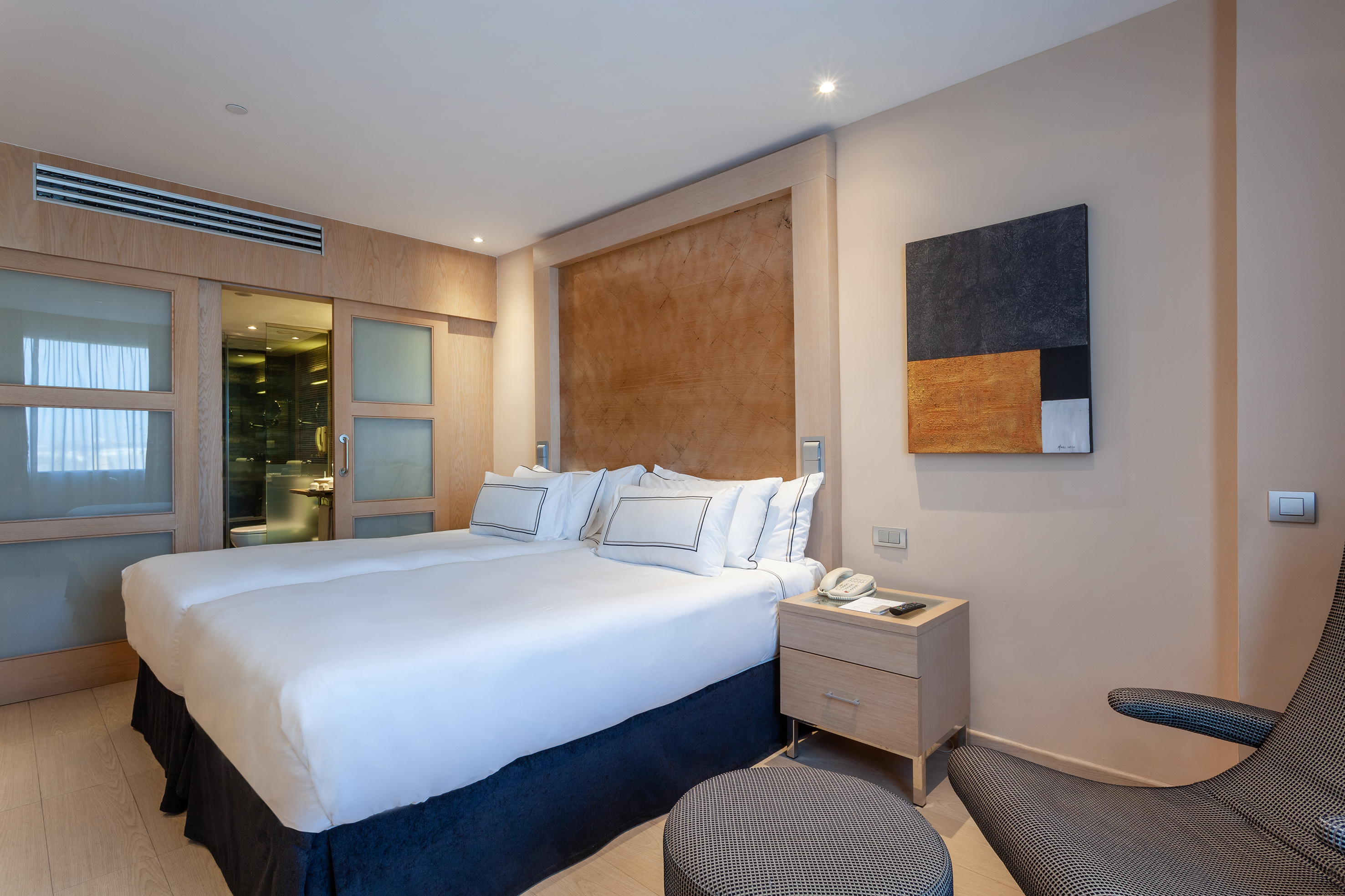 Modern hotel room with twin beds, wooden headboard, and ensuite bathroom.