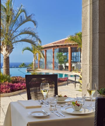 a table set for a meal outside with a pool and palm trees