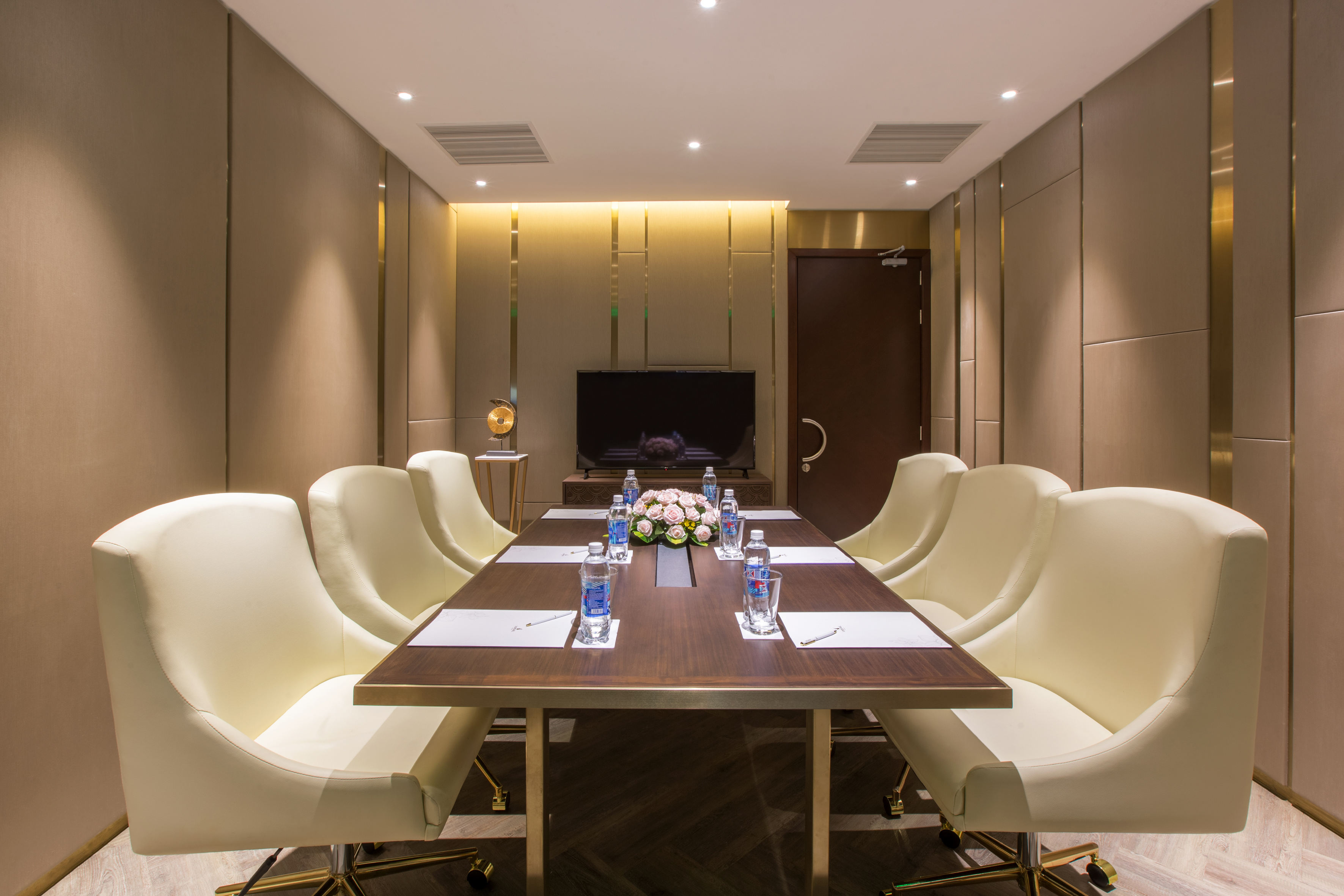 Elegant conference room with long wooden table, cream chairs, and TV.