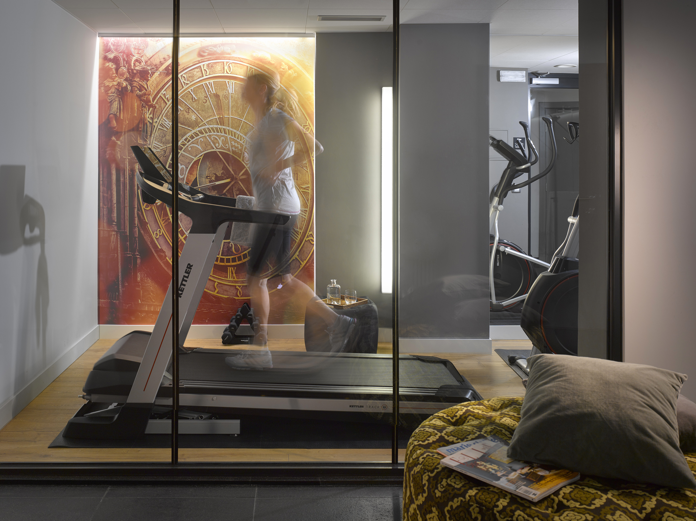 Woman running on treadmill in modern hotel gym with large clock mural.