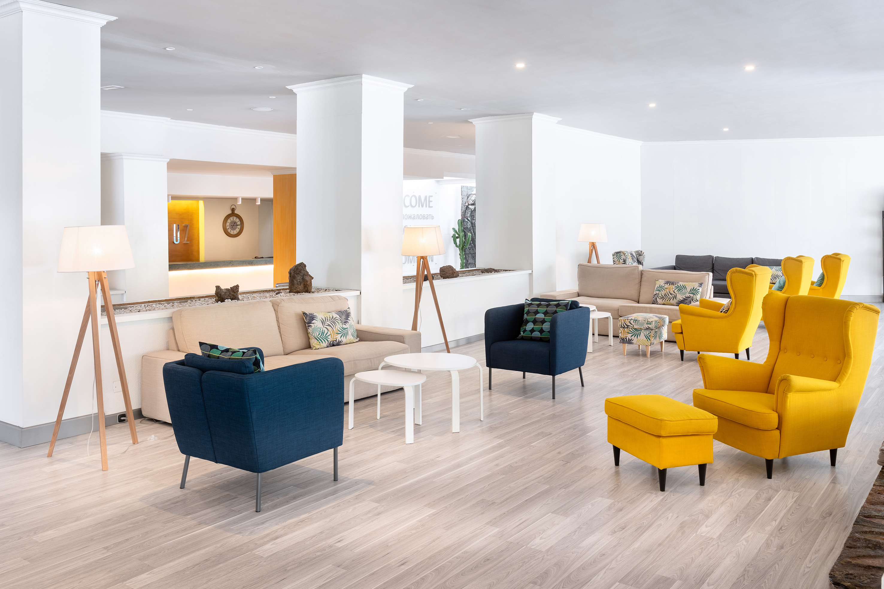 Modern hotel lobby with yellow armchairs, blue chairs, and beige sofas.