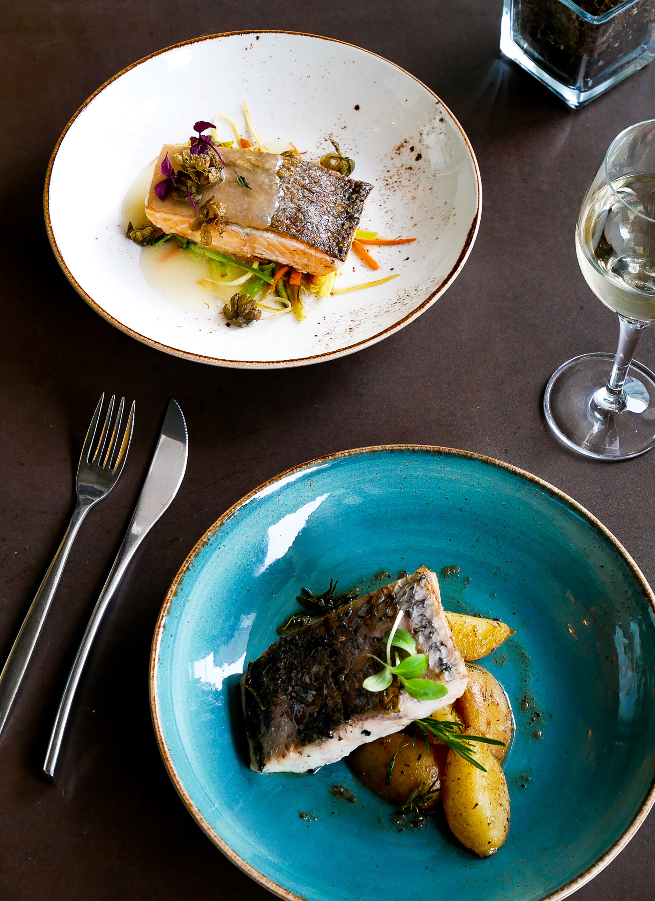 Gourmet salmon and seabass dishes with vegetables, potatoes, and white wine.
