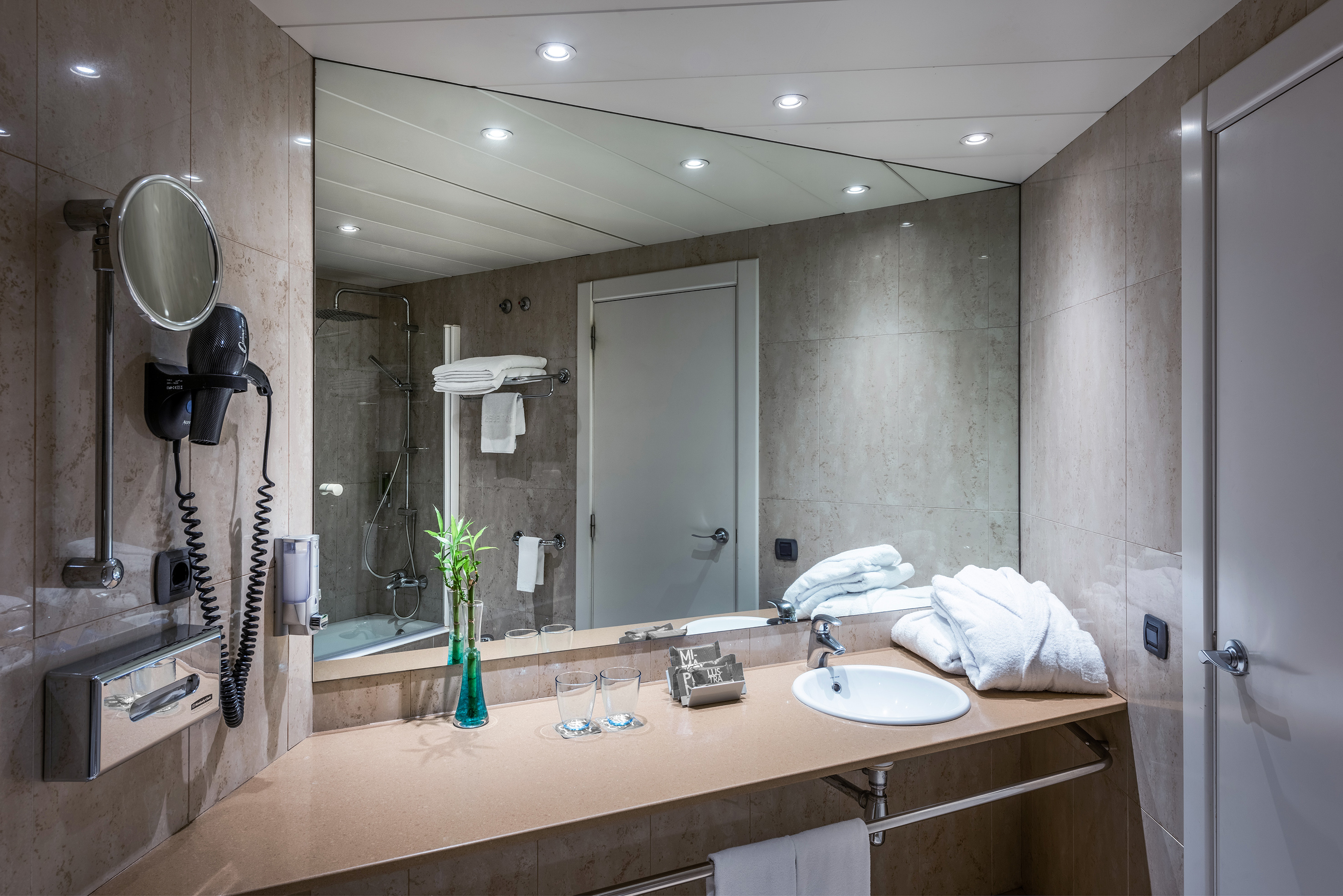 Modern hotel bathroom vanity with large mirror, sink, shower, and fresh towels.