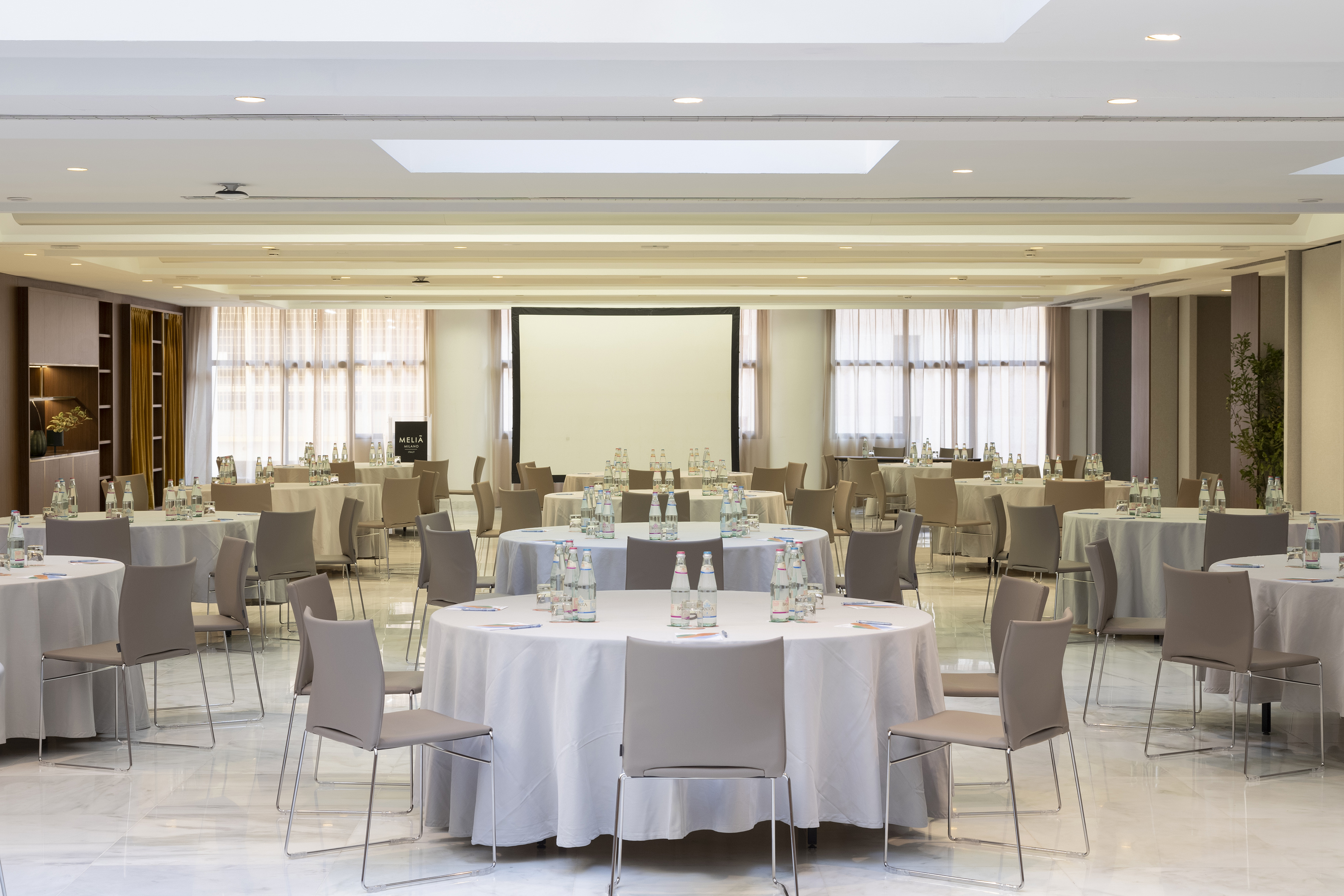 Meliá Milano conference room with round tables, chairs, and projector screen.