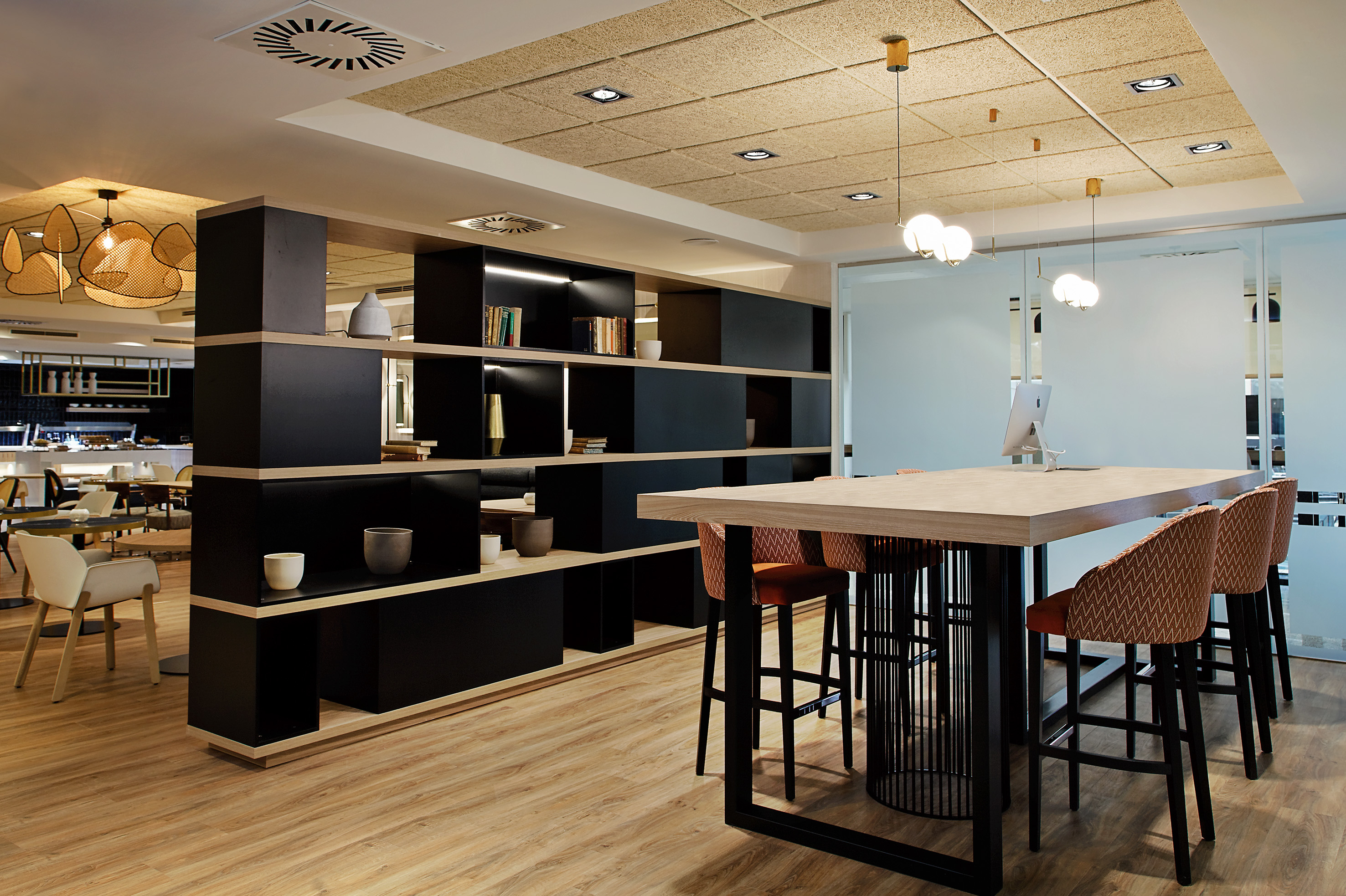 Modern hotel lounge with communal table, high stools, and stylish room divider.