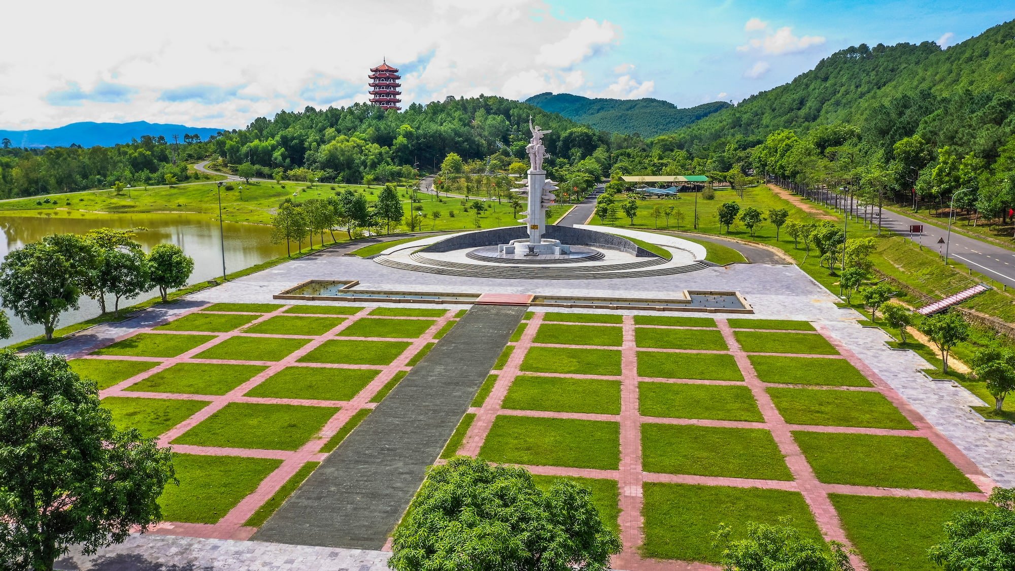 a large white statue in a park with a pond and trees