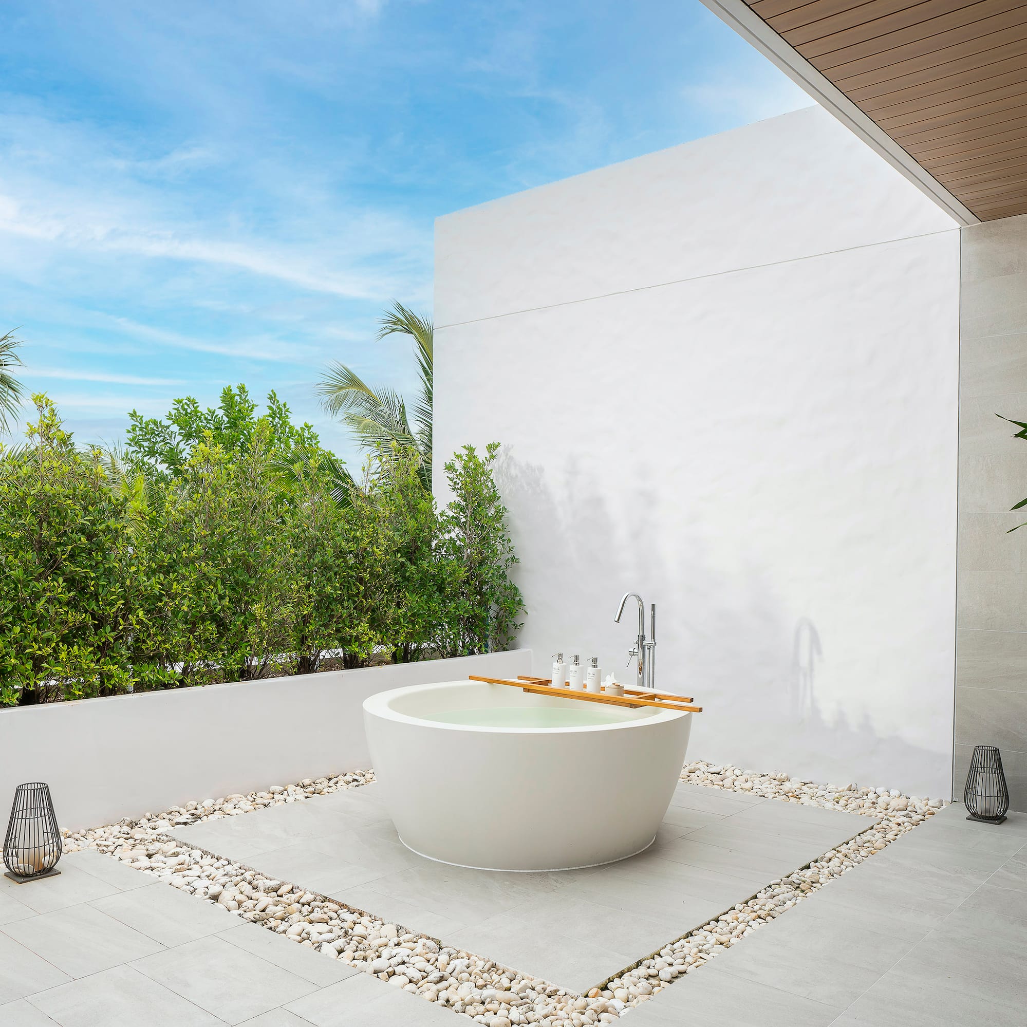 a bathtub outside with a white wall and plants