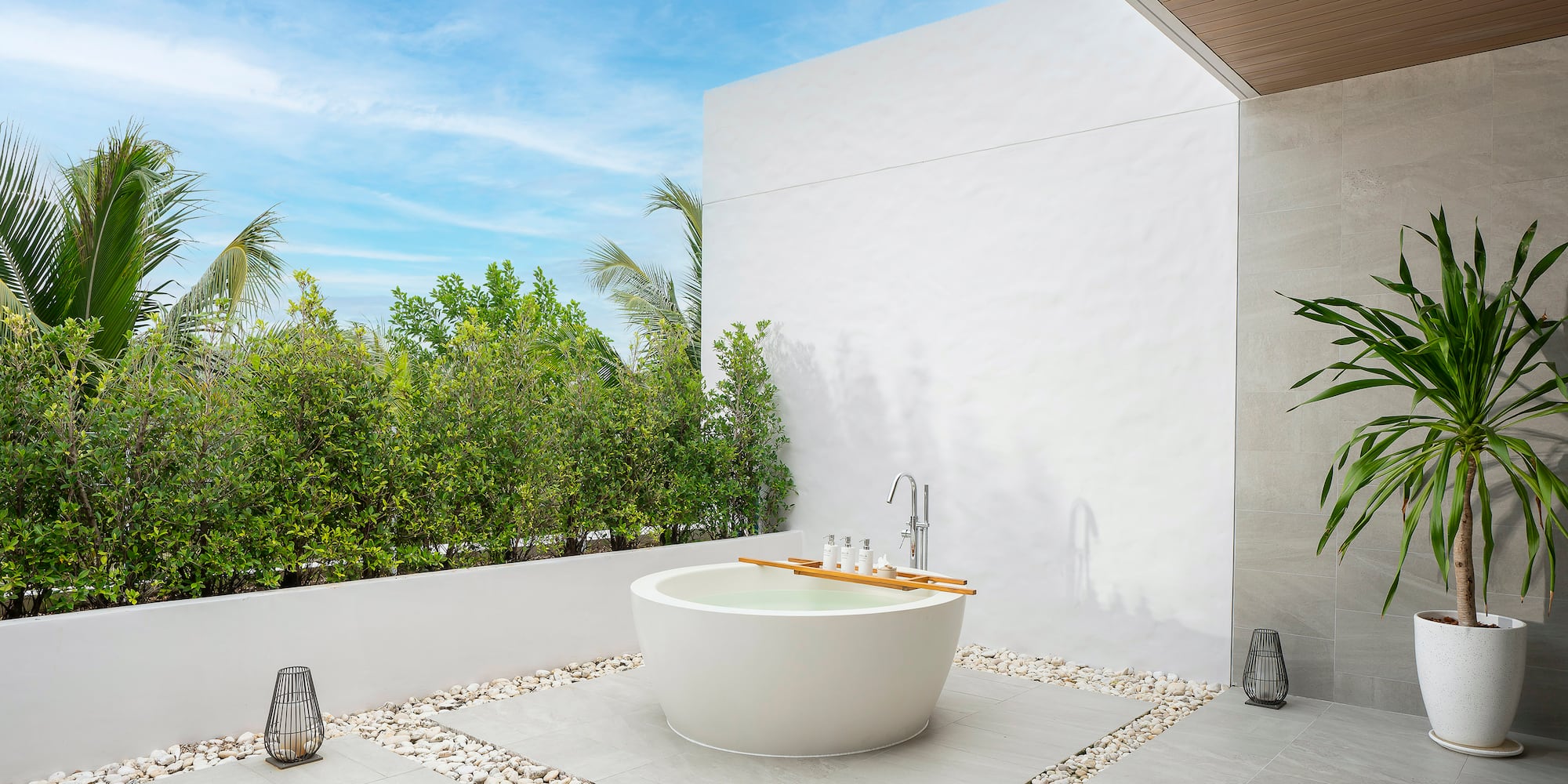 a bathtub outside with a white wall and plants