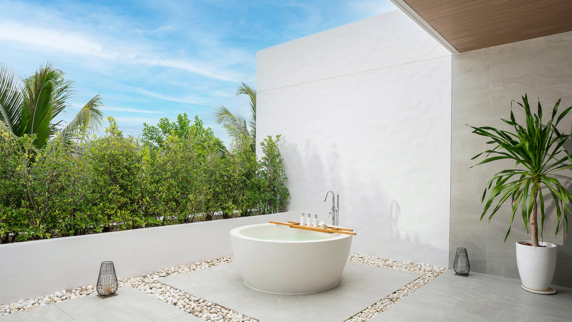 a bathtub outside with a white wall and plants
