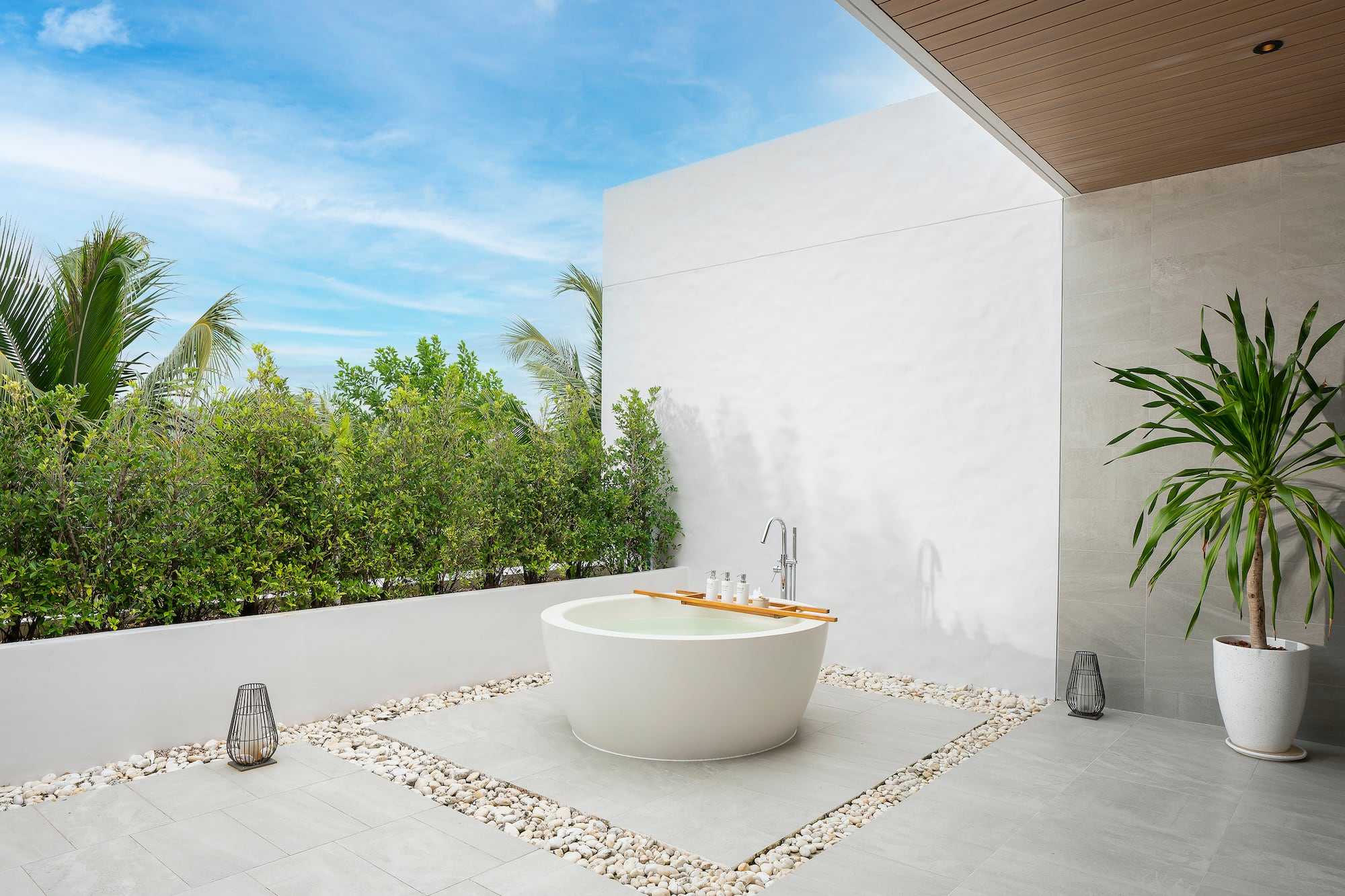 a bathtub outside with a white wall and plants