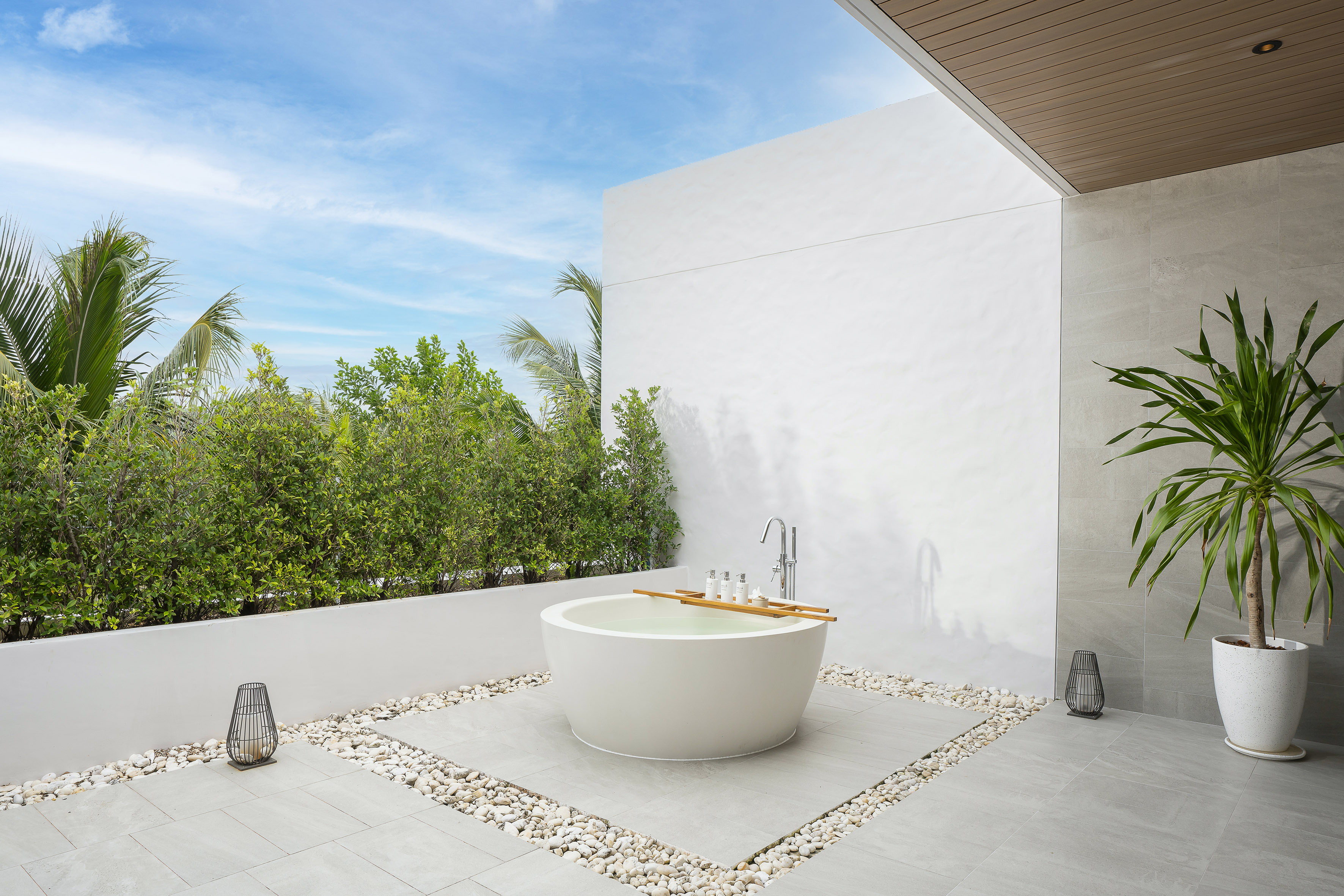 Outdoor freestanding bathtub on modern patio with tropical plants.
