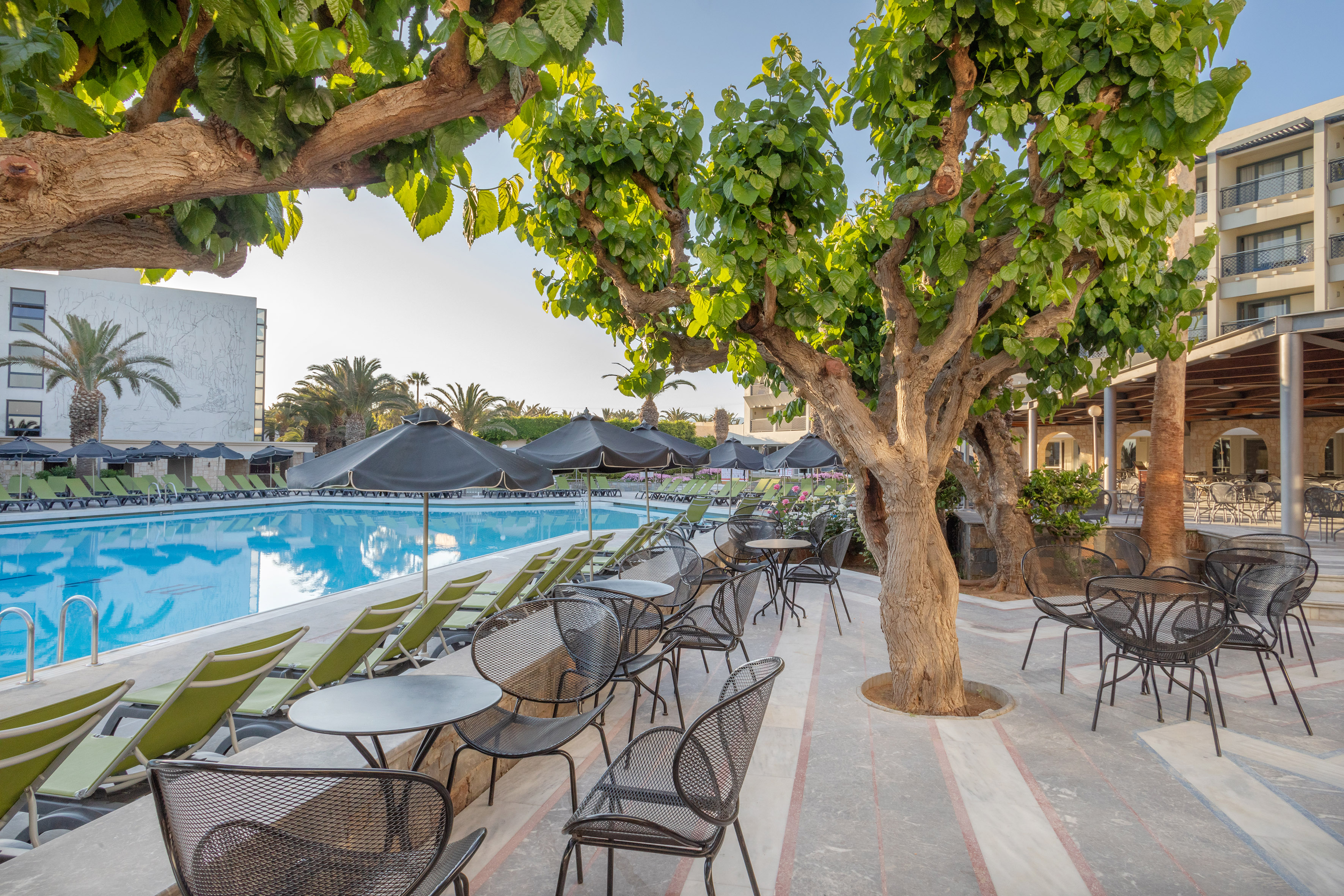 Shaded resort pool area with green loungers and outdoor dining patio.