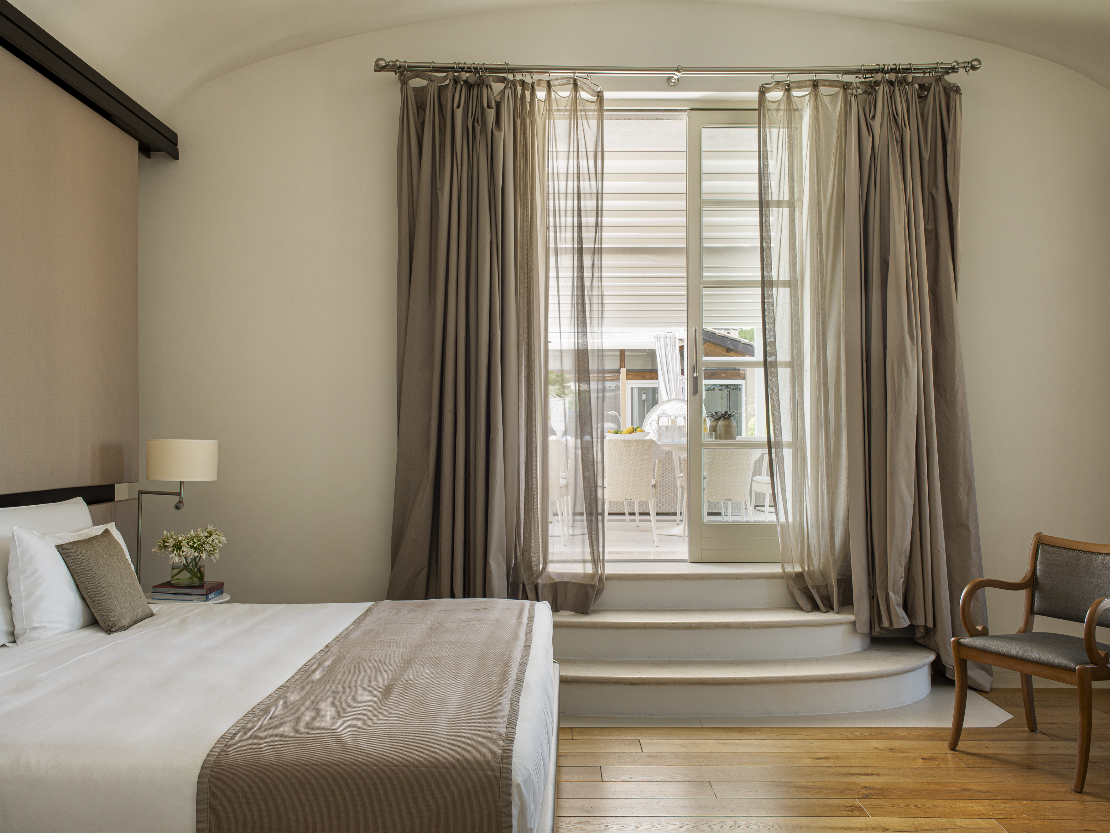 Hotel bedroom with bed, wood floor, and steps to a sunlit patio.