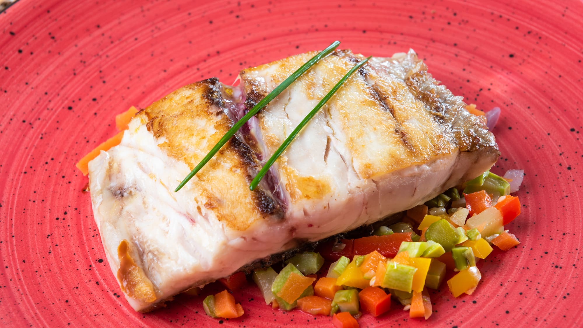 a piece of fish with vegetables on a red plate