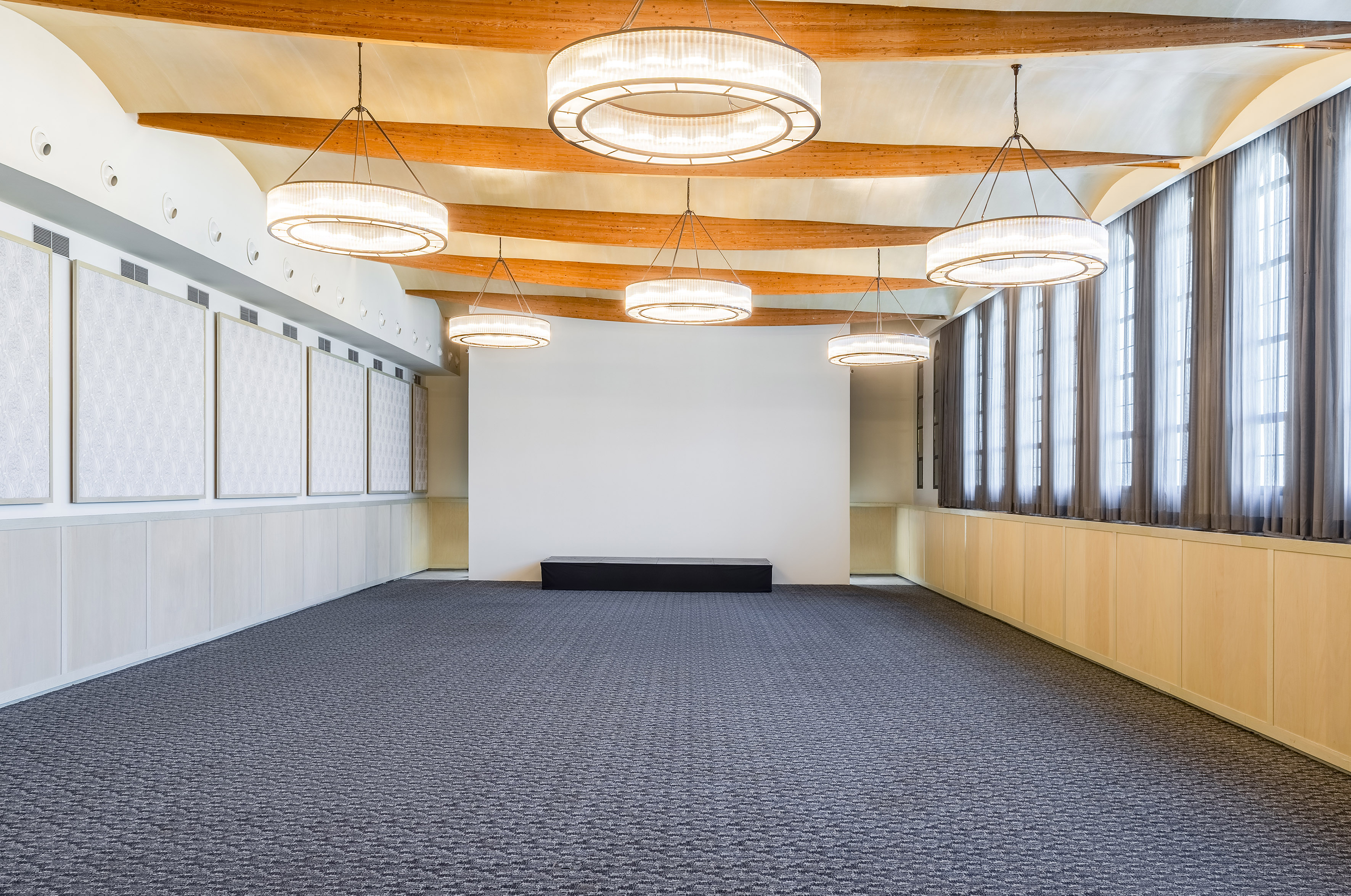 Modern event hall with chandeliers, wooden beams, and patterned carpet.