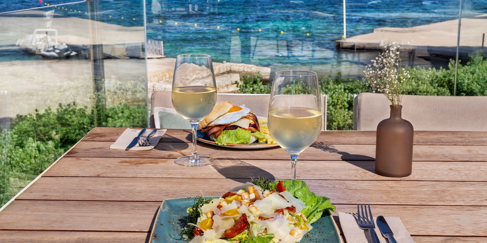 a plate of salad and wine glasses on a table with a body of water in the background