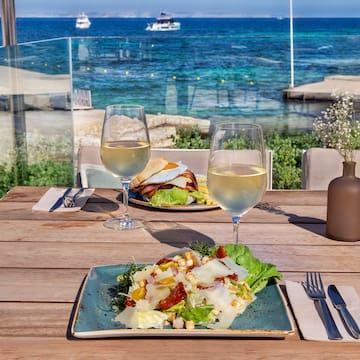 a plate of salad and wine glasses on a table with a body of water in the background