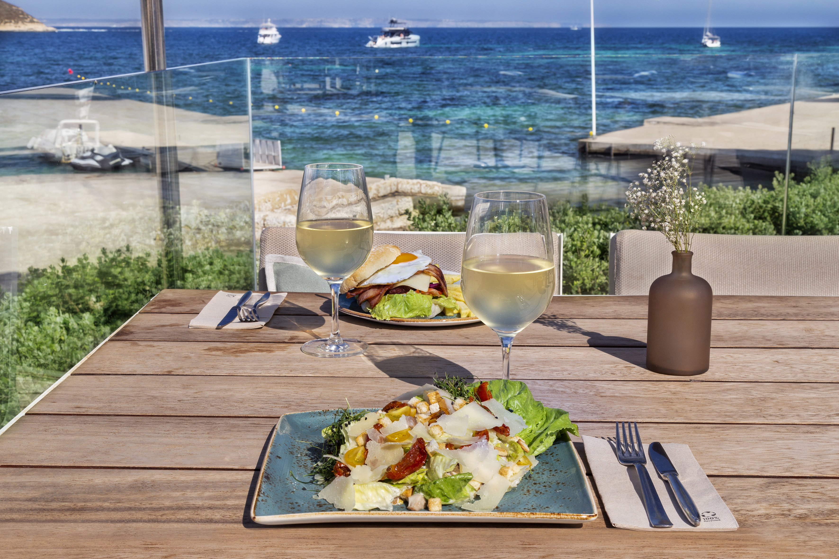 Seaside dining with Caesar salad, burger, white wine, and ocean view.