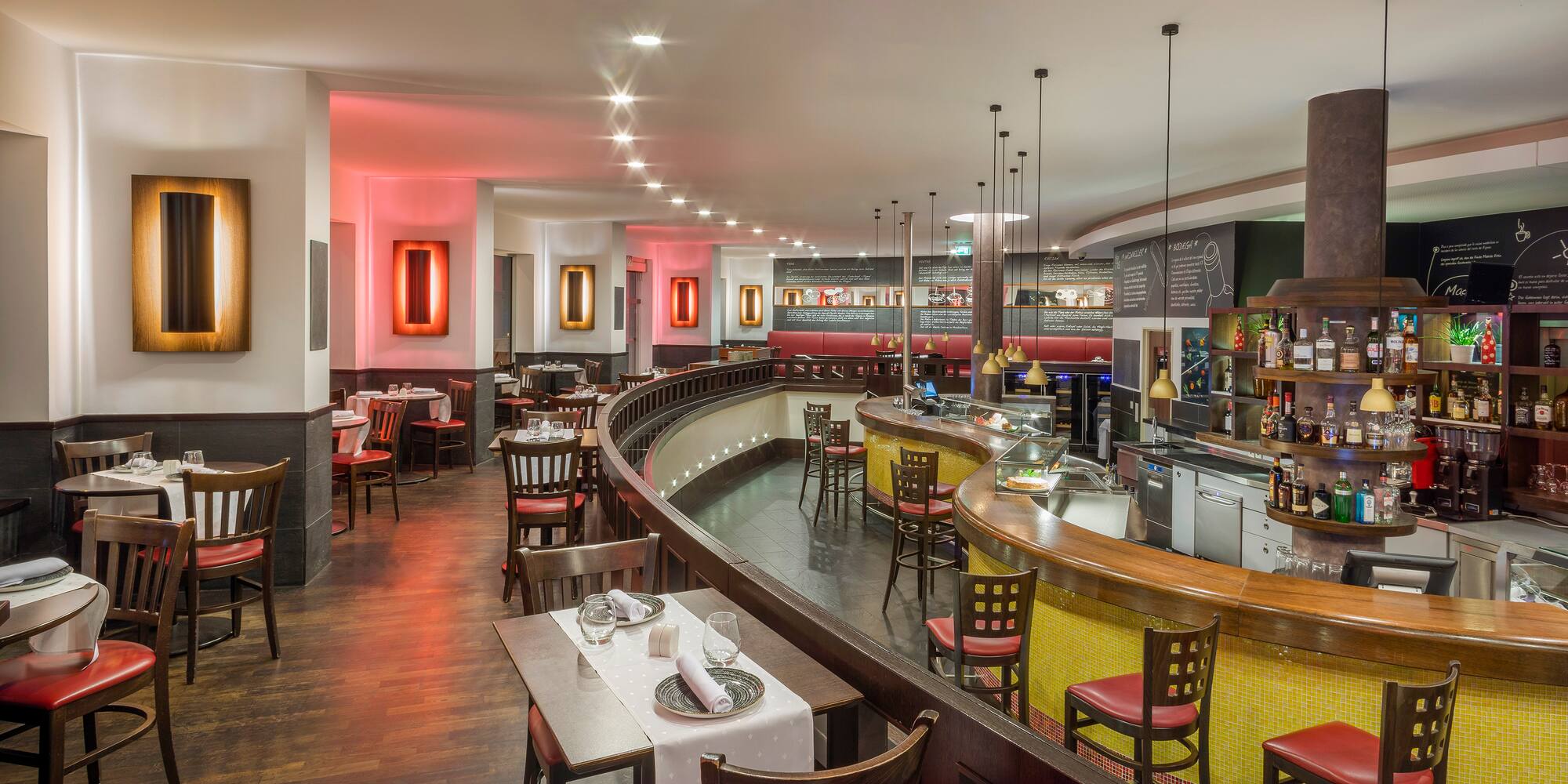 Modern restaurant interior with curved bar, red barstools, and set dining tables.