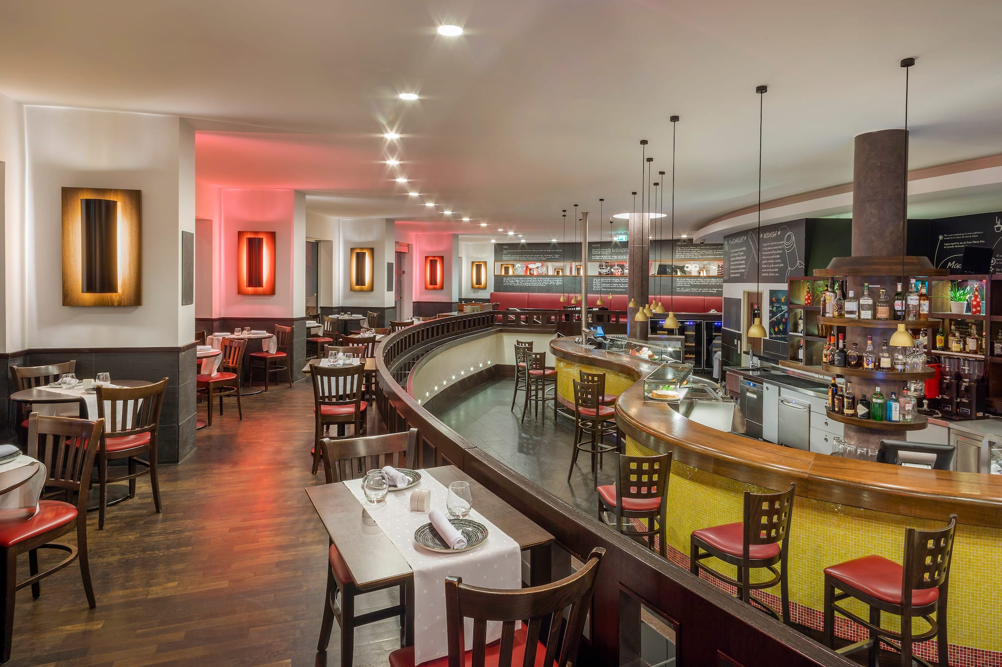 Modern restaurant dining area and bar with curved design and red chairs.