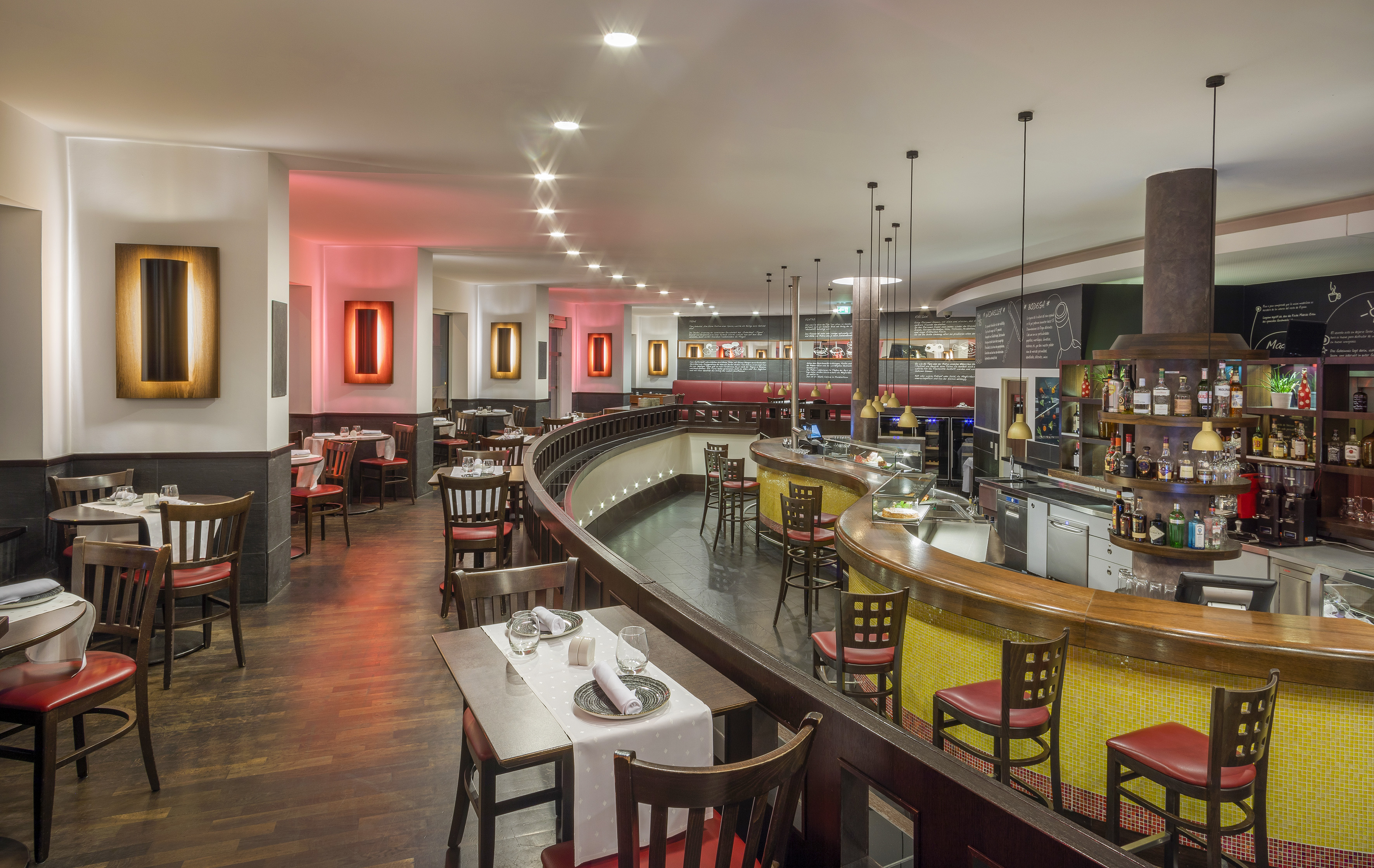 Modern restaurant dining area and bar with curved design and red chairs.