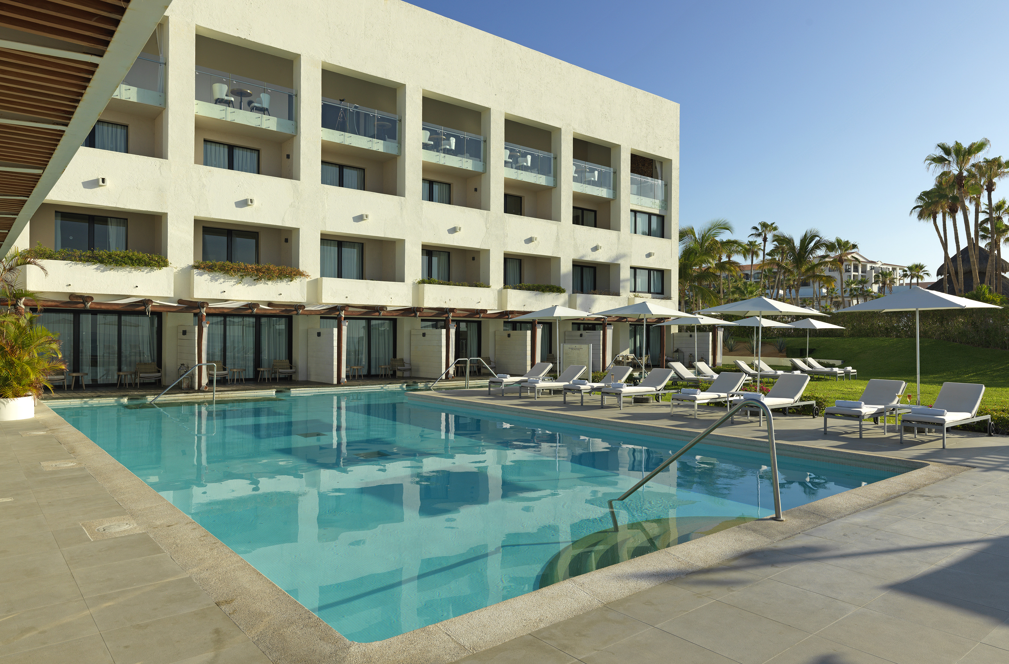 Modern resort hotel with blue swimming pool, lounge chairs, and palm trees.