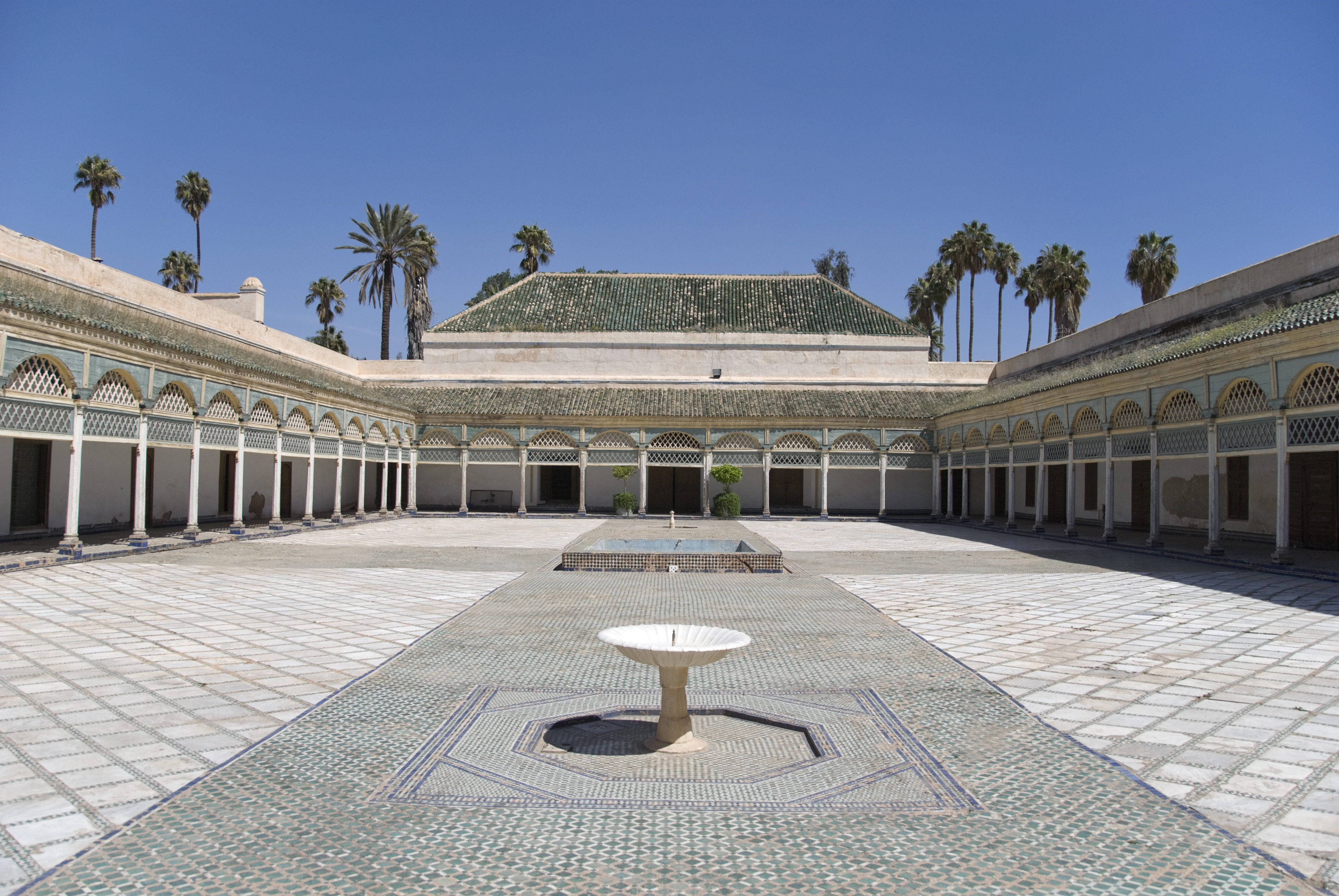 a courtyard with a fountain and palm trees with Bahia Palace in the background