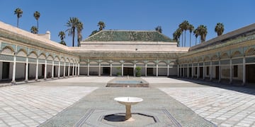a courtyard with a fountain and palm trees with Bahia Palace in the background